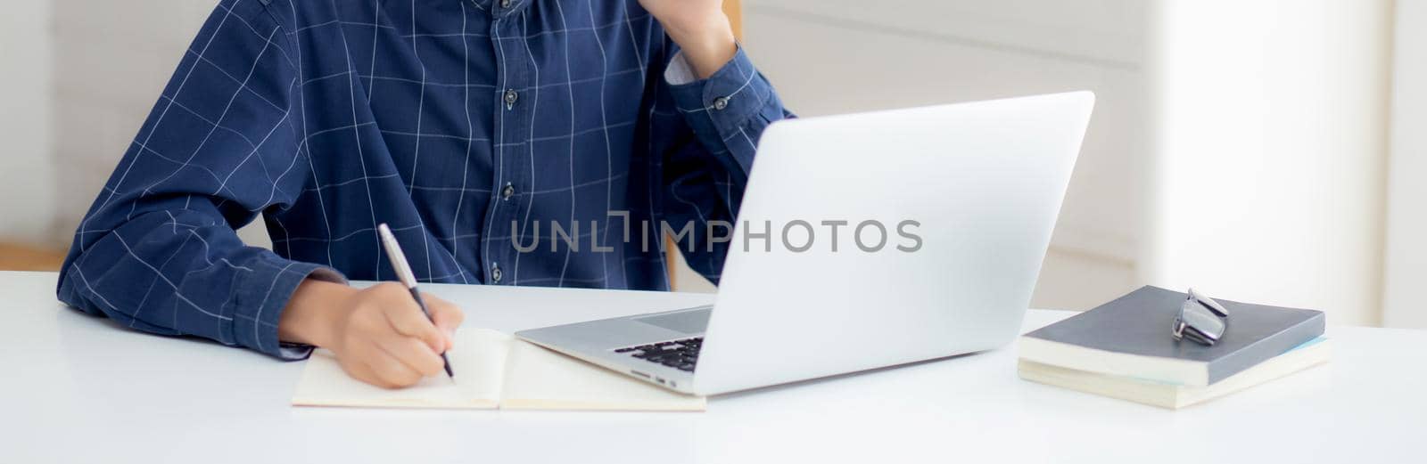 Young asian business man in face mask talking smartphone and work on laptop computer for protect covid-19, businessman quarantine work from home and writing notebook, social distancing and stay home.