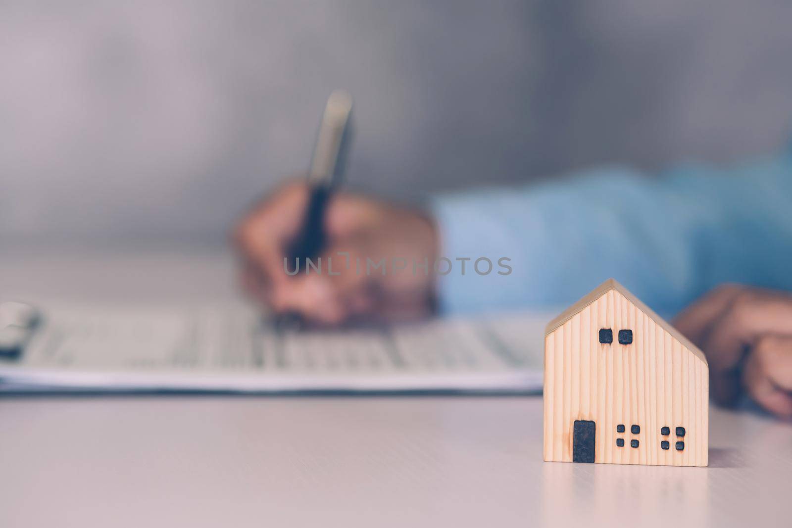 Real estate agent holding home and signing contract about agreement of real property on desk, house broker and planning investment, businessman writing on document form rent house, business concept. by nnudoo