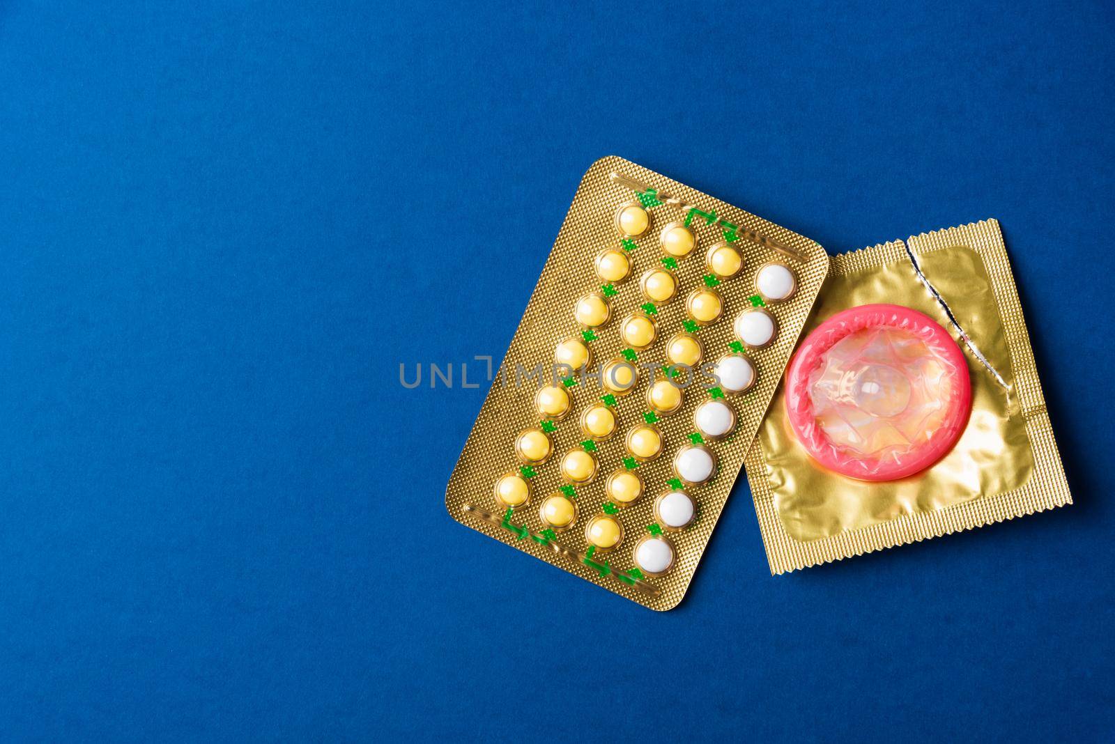 World sexual health or Aids day, condom on wrapper pack and contraceptive pills blister hormonal birth control pills, studio shot isolated on a dark blue background, Safe sex and reproductive health concept