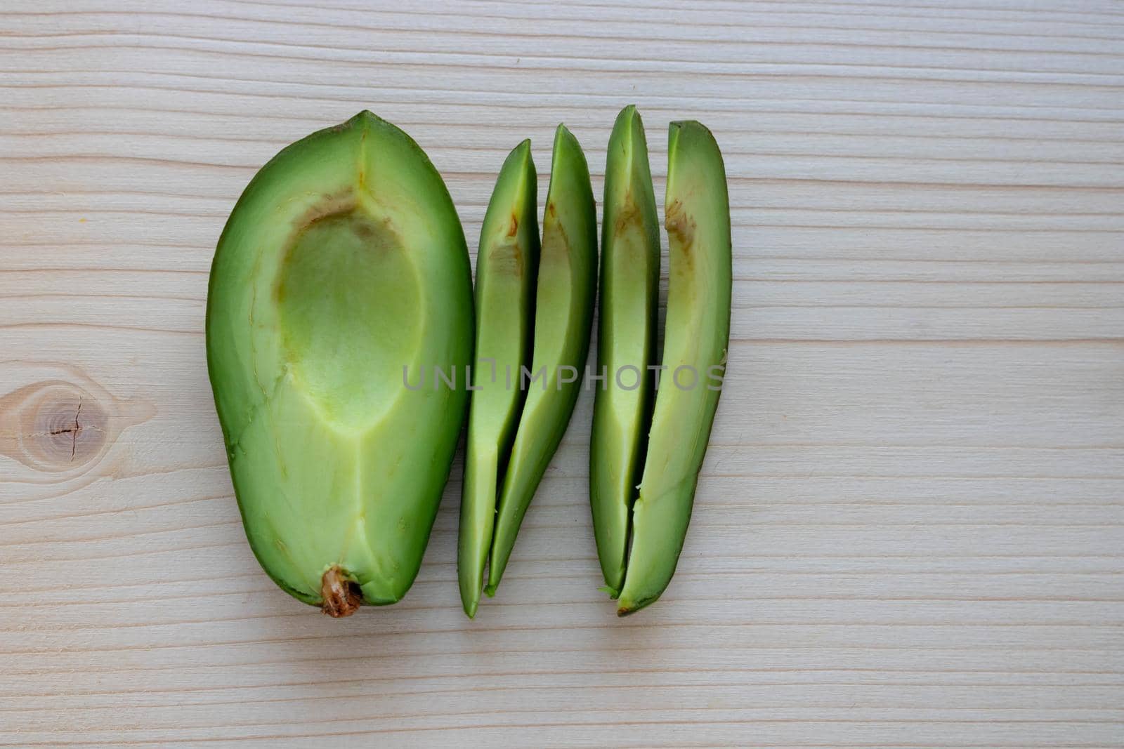 Slices of ripe avocado lie on a light cutting board.