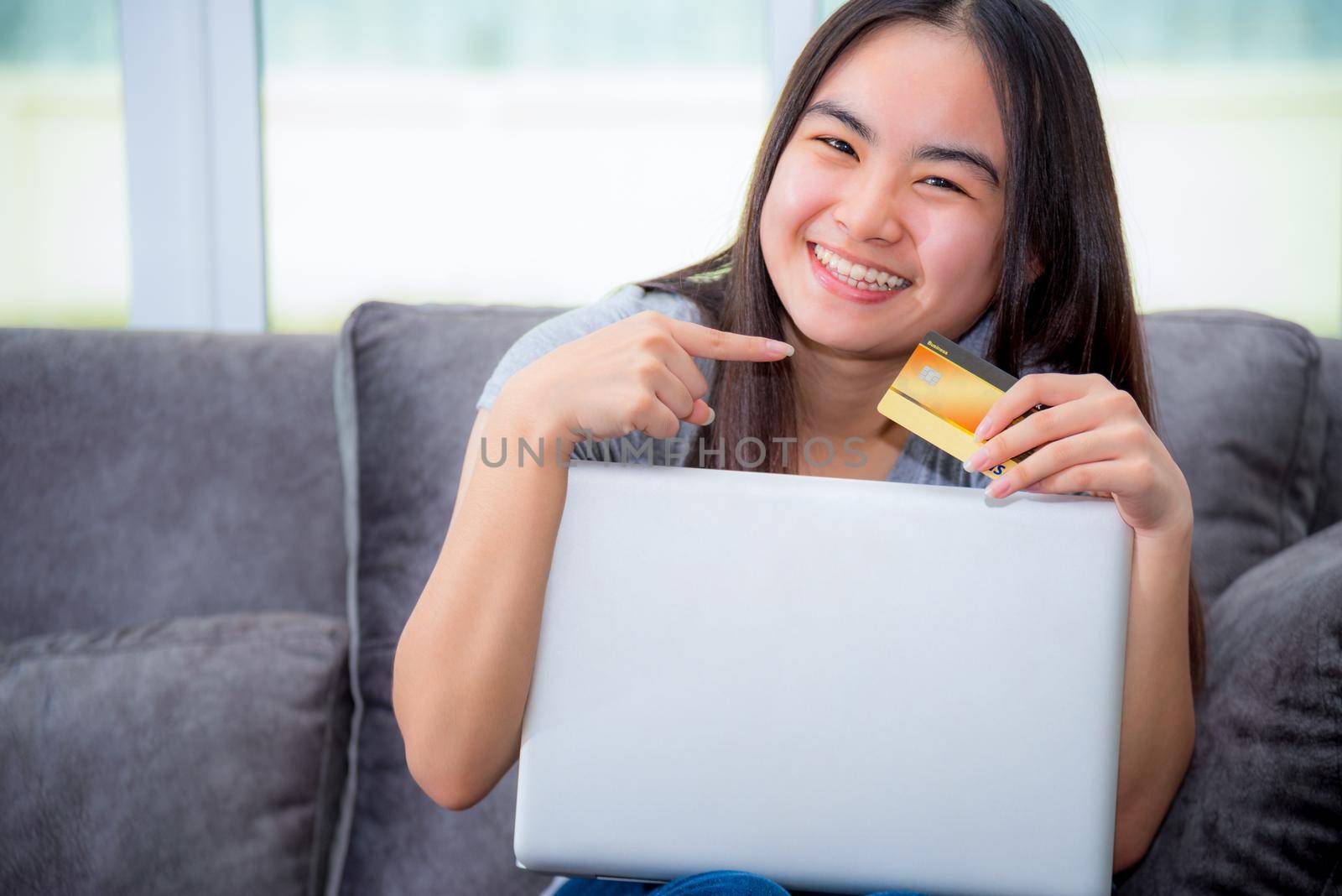 Asian young woman holding SME credit card use a laptop computer buy products payment shopping online, Cute teenage girl smile pointing finger at credit card happy lifestyle through credit card payment