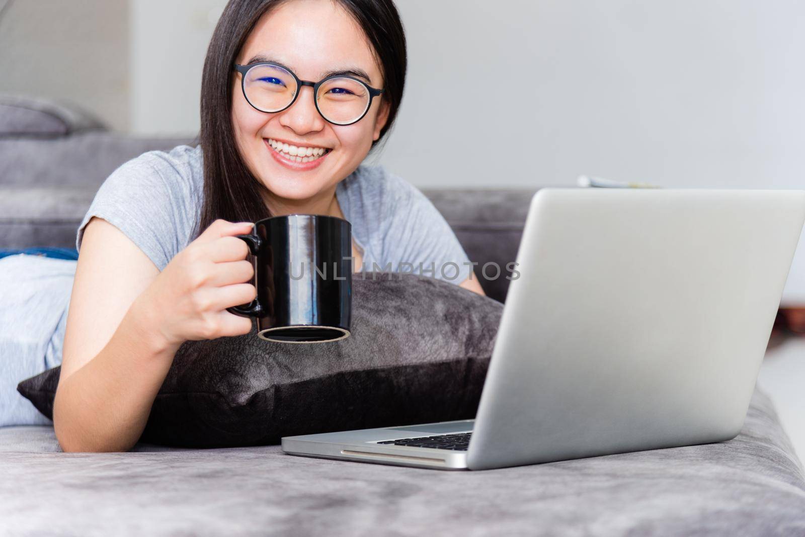 Portrait beautiful Asian young woman holding coffee cup smile and looking during a work, Cute girl teens happy on the sofa working remotely with a laptop and internet computer communication from home