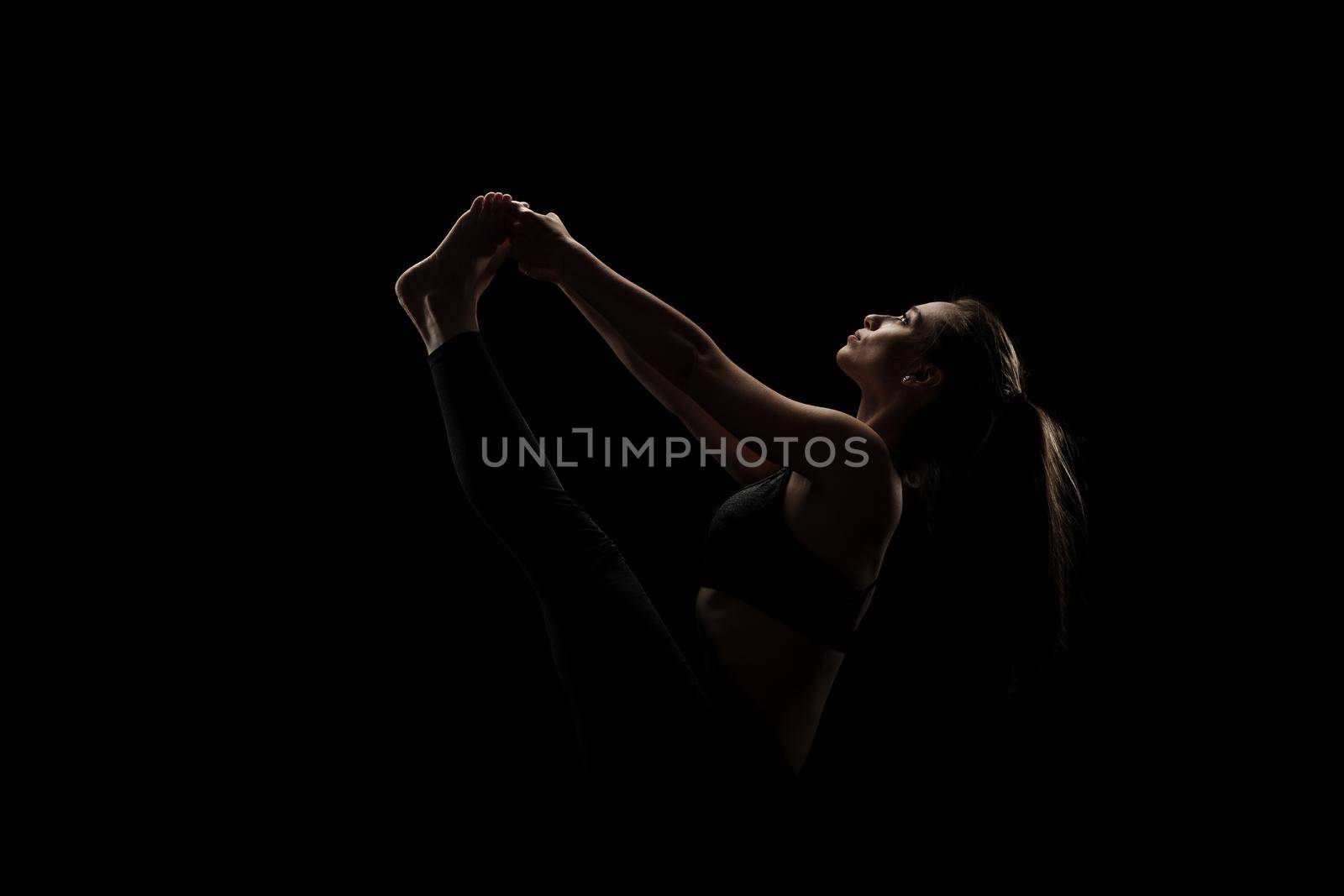 cute caucasian girl exercising yoga poses against dark backgroung. side lit silhouette.