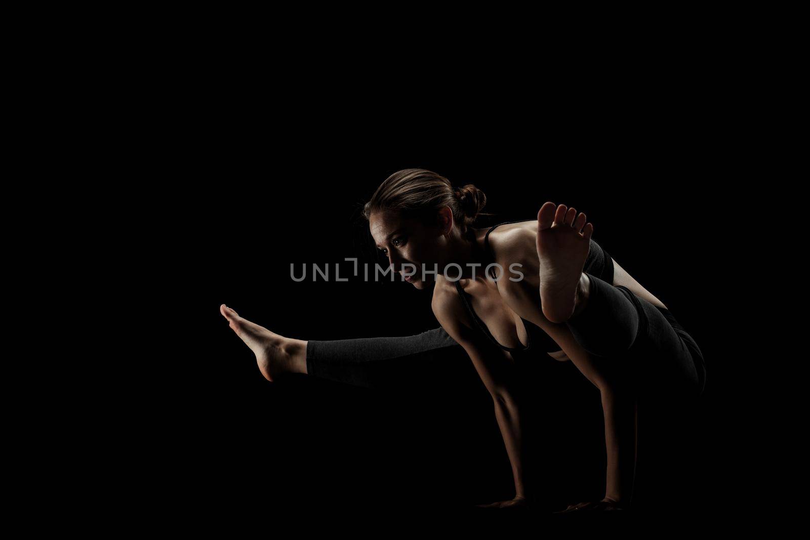 cute caucasian girl exercising yoga poses against dark backgroung. side lit silhouette.