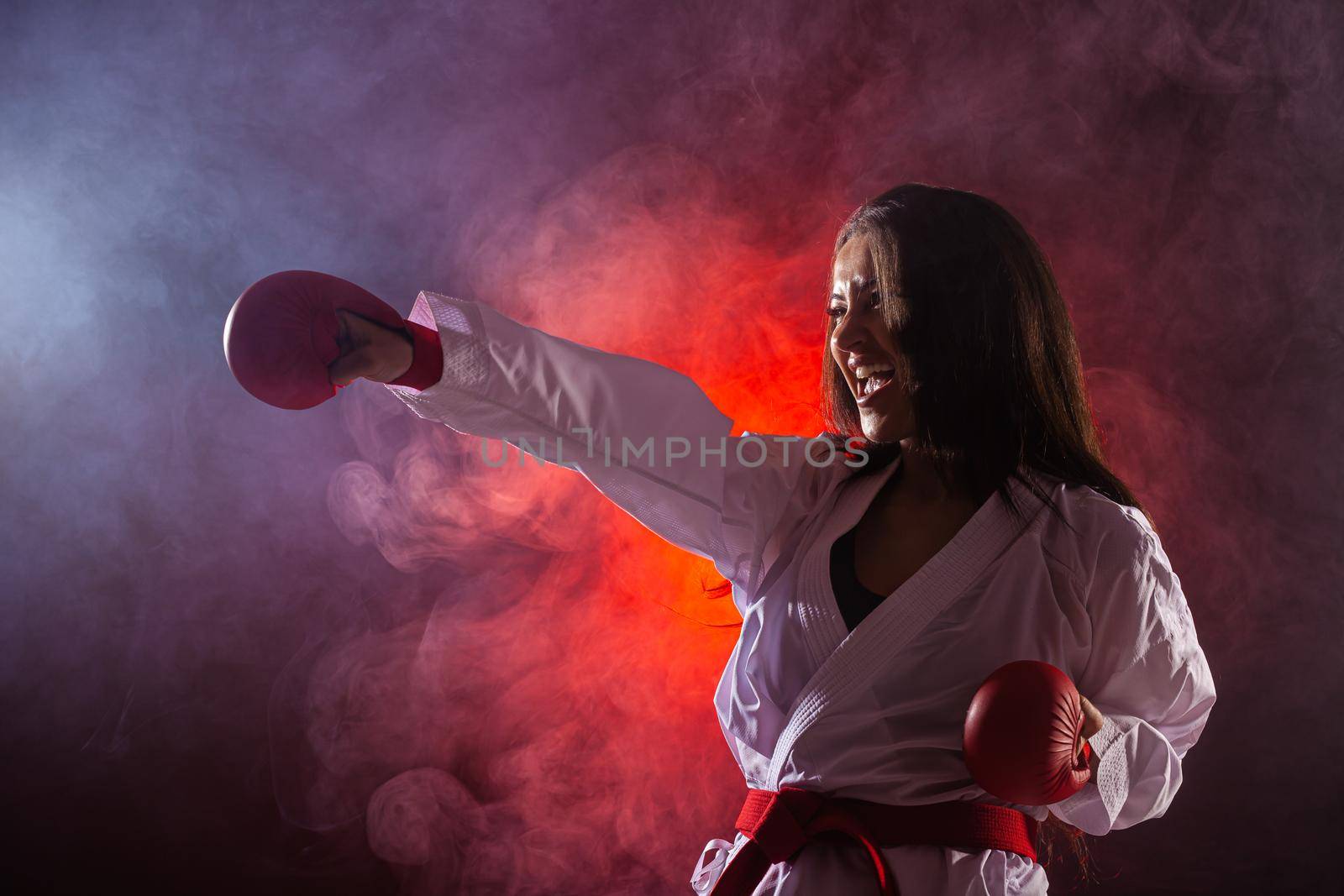 girl exercising karate punch against red fog background. by kokimk