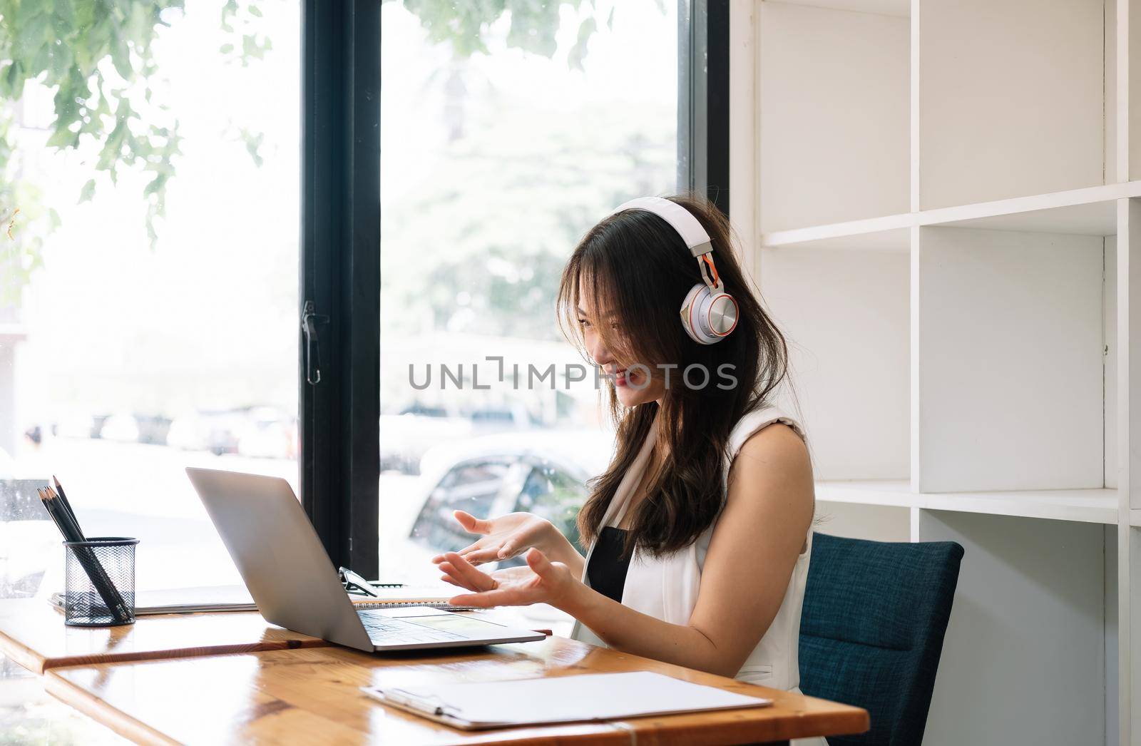 Side view of business woman communicates by video conference. Asian female using laptop computer for group meeting by nateemee