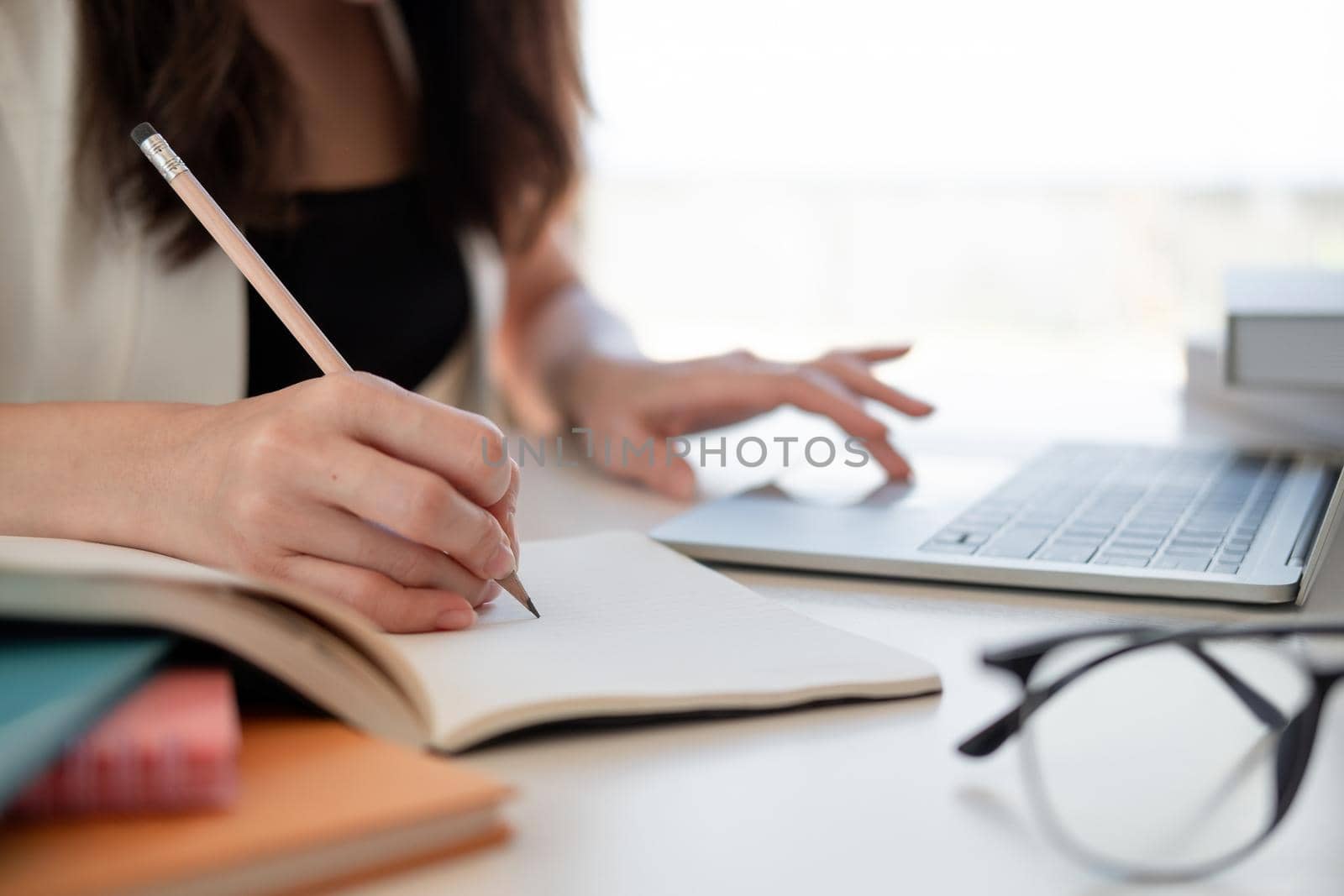 Close up woman's hands with laptop computer, notebook and pen taking notes in business office by nateemee