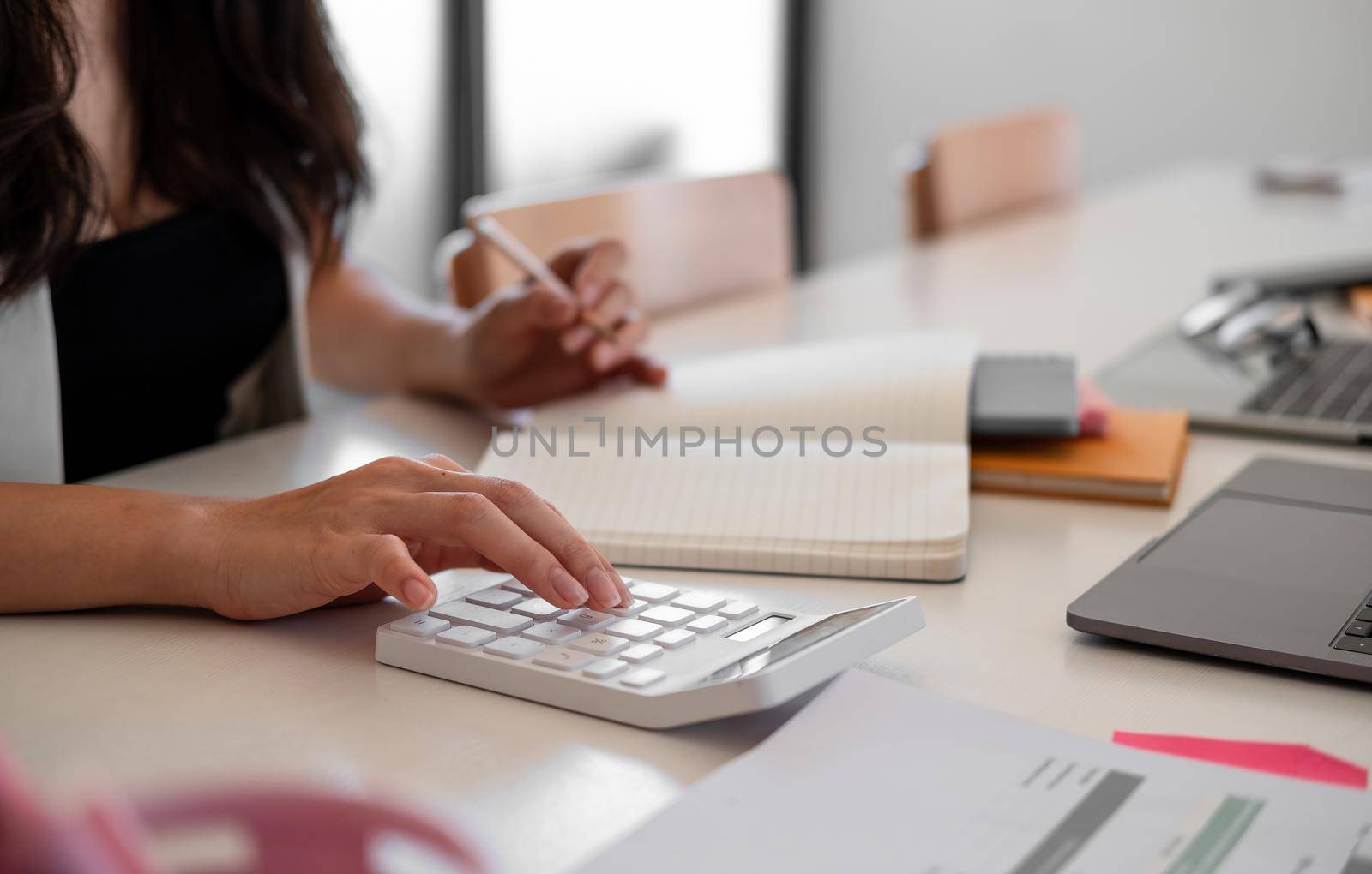 Business woman with calculator counting making notes at office hand is writes in a notebook at home office by nateemee