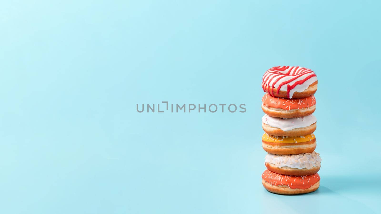 Stack of assorted donuts on blue background. Many colorful glazed doughnut with sprinkles stacked with copy space. Long horizontal banner
