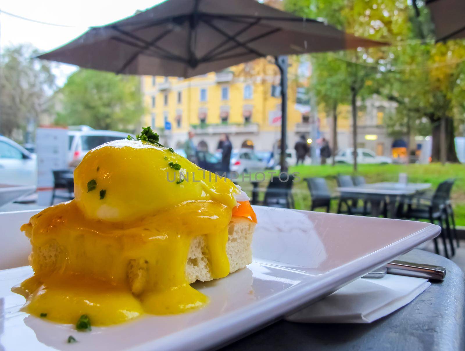 Sunny breakfast with bread toast, salmon and poached egg with greens on a rainy day in Italy