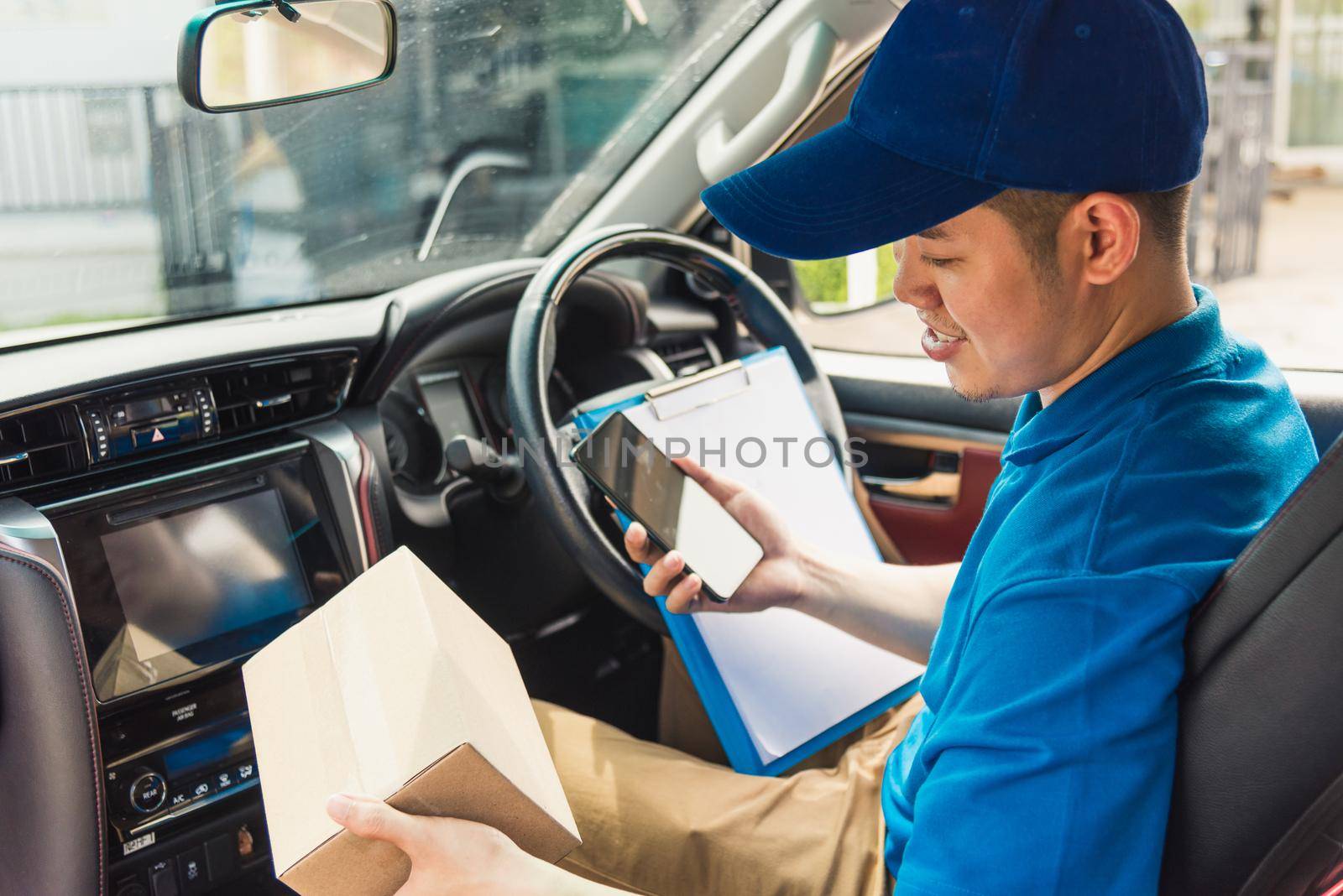 delivery man courier online holding deliveries out boxes inside the car and using mobile smartphone checking location by Sorapop