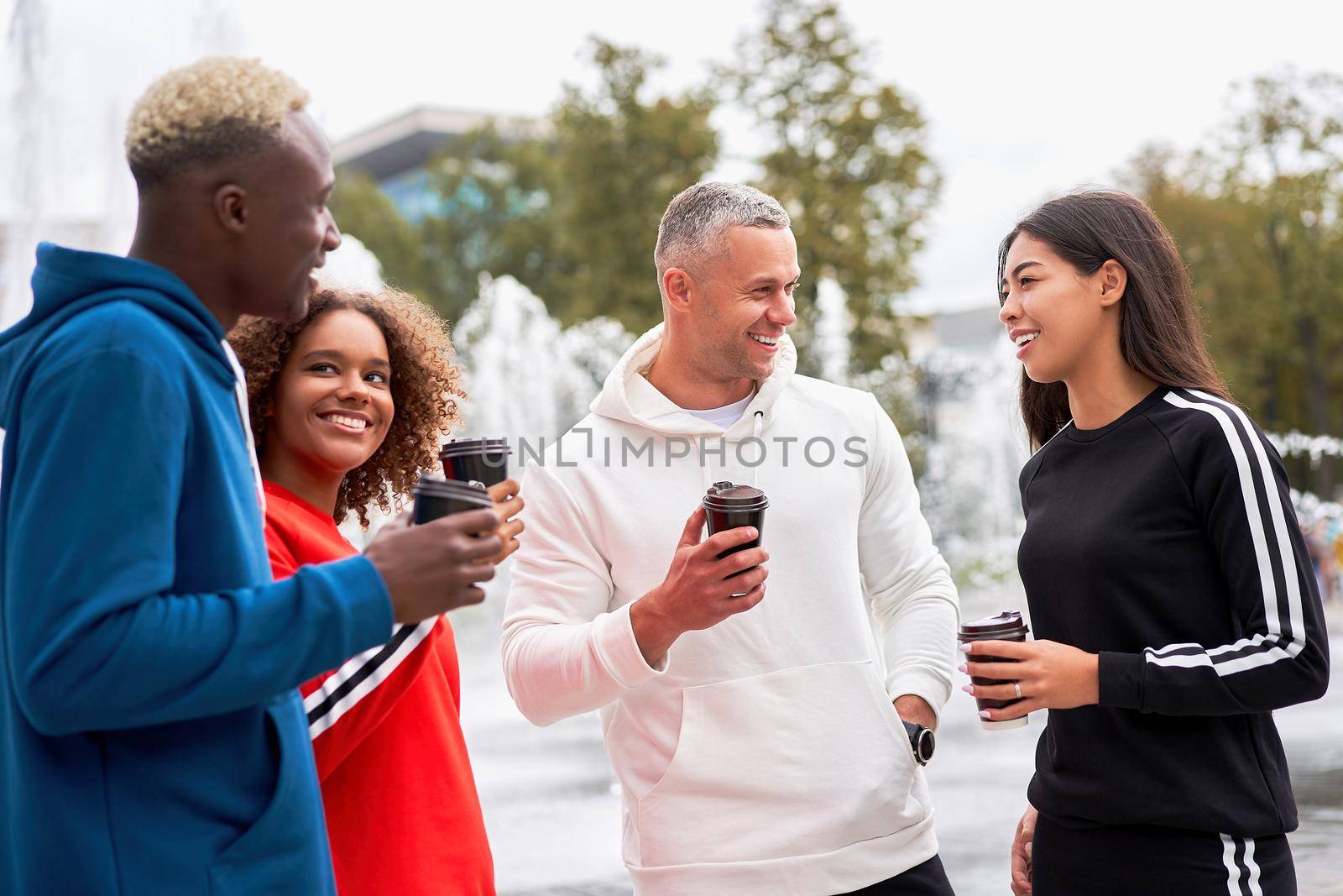 Multi-ethnic group teenage friends. African-american asian caucasian student spending time together Multiracial friendship Happy smiling People dressed colorful sportswear drink coffee outdoor