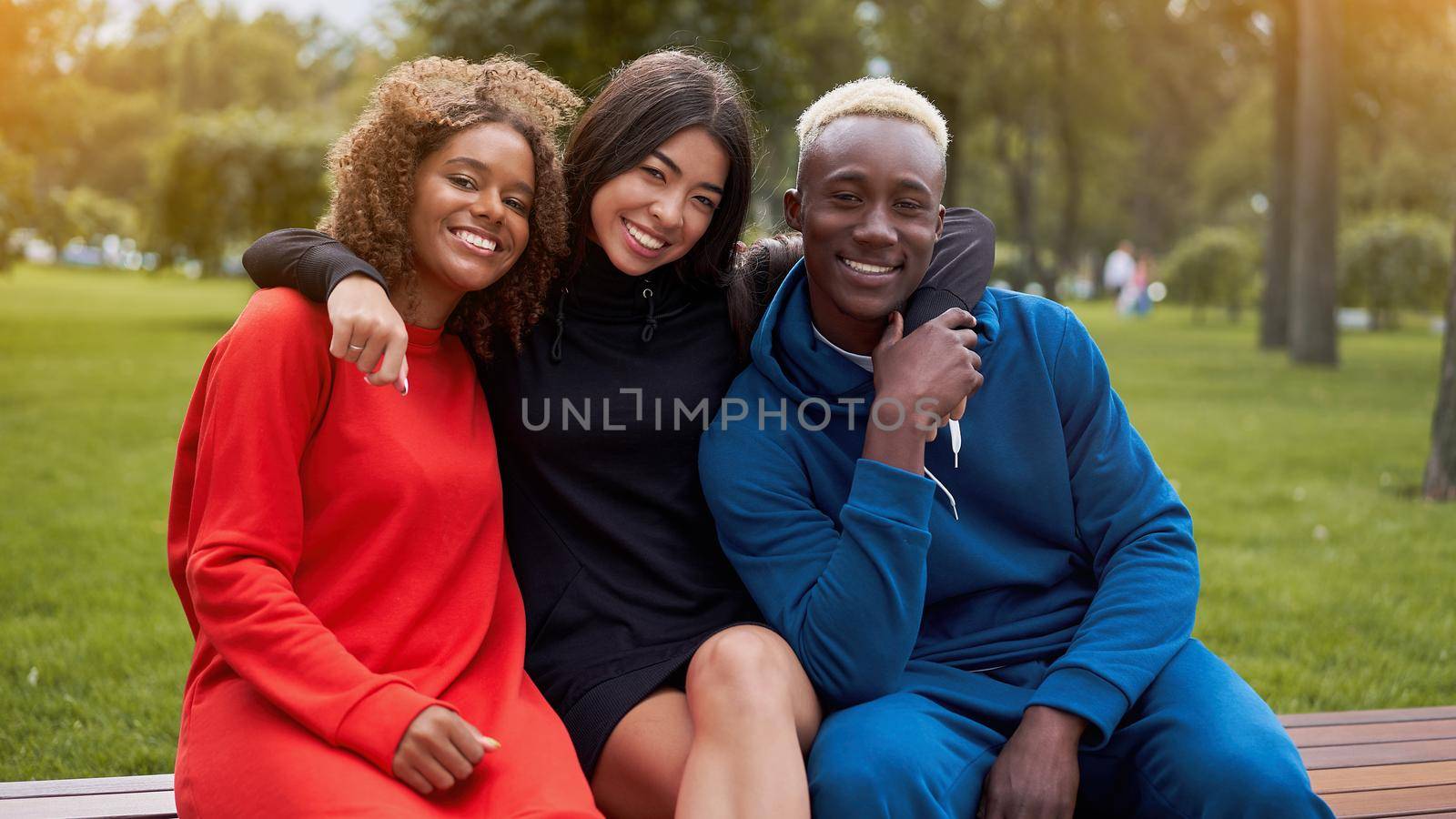 Multi-ethnic group teenage friends. African-american asian student spending time together Multiracial friendship Happy smiling People dressed colorful sportswear sitting bench park outdoor
