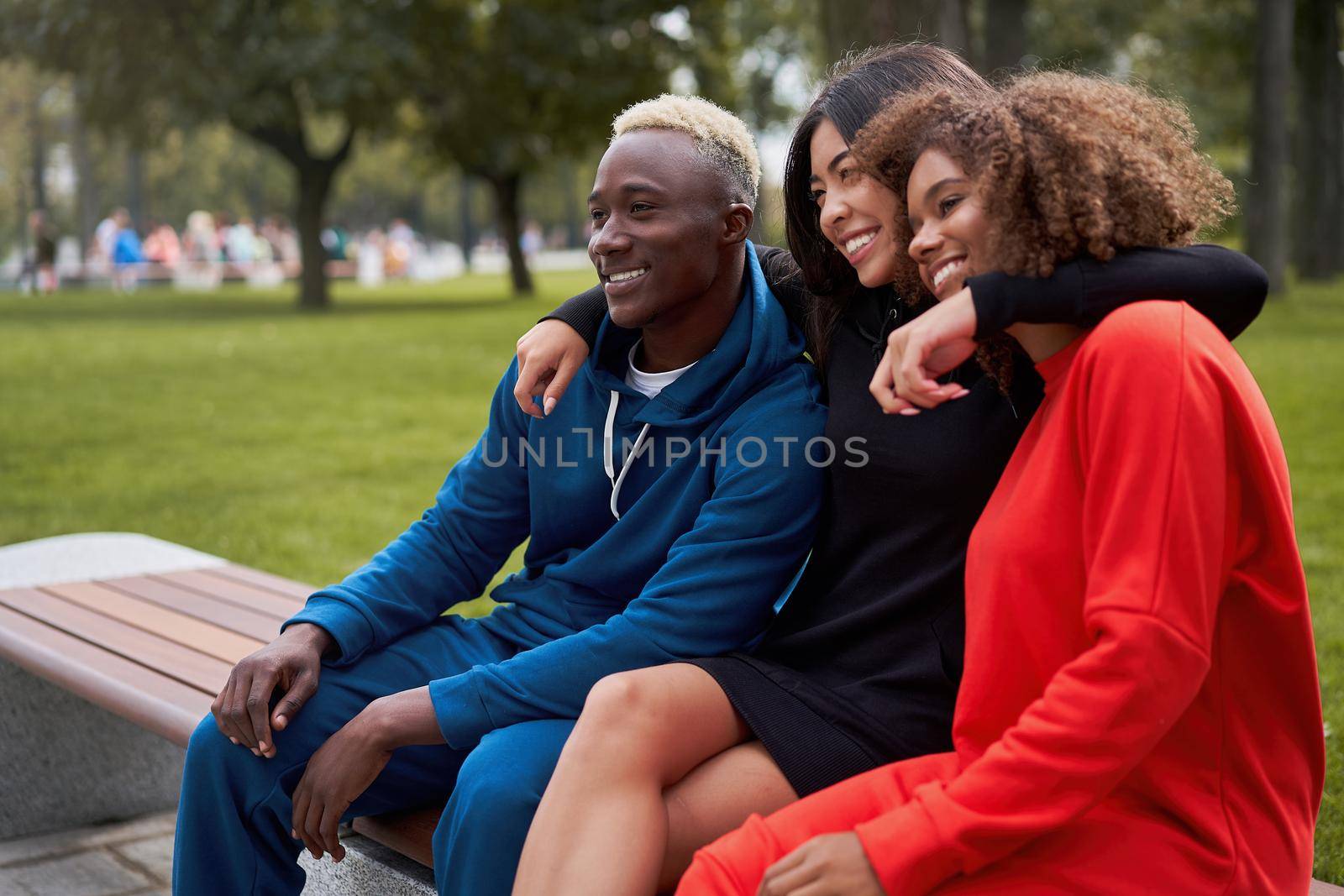 Multi-ethnic group teenage friends. African-american asian student spending time together Multiracial friendship Happy smiling People dressed colorful sportswear sitting bench park outdoor