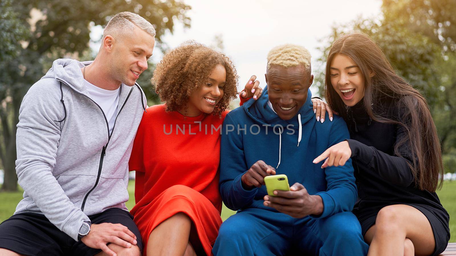 Multi ethnic friends outdoor looking smartphone screen. Diverse group people Afro american asian caucasian spending time together Multiracial male female student sitting bench park outdoors