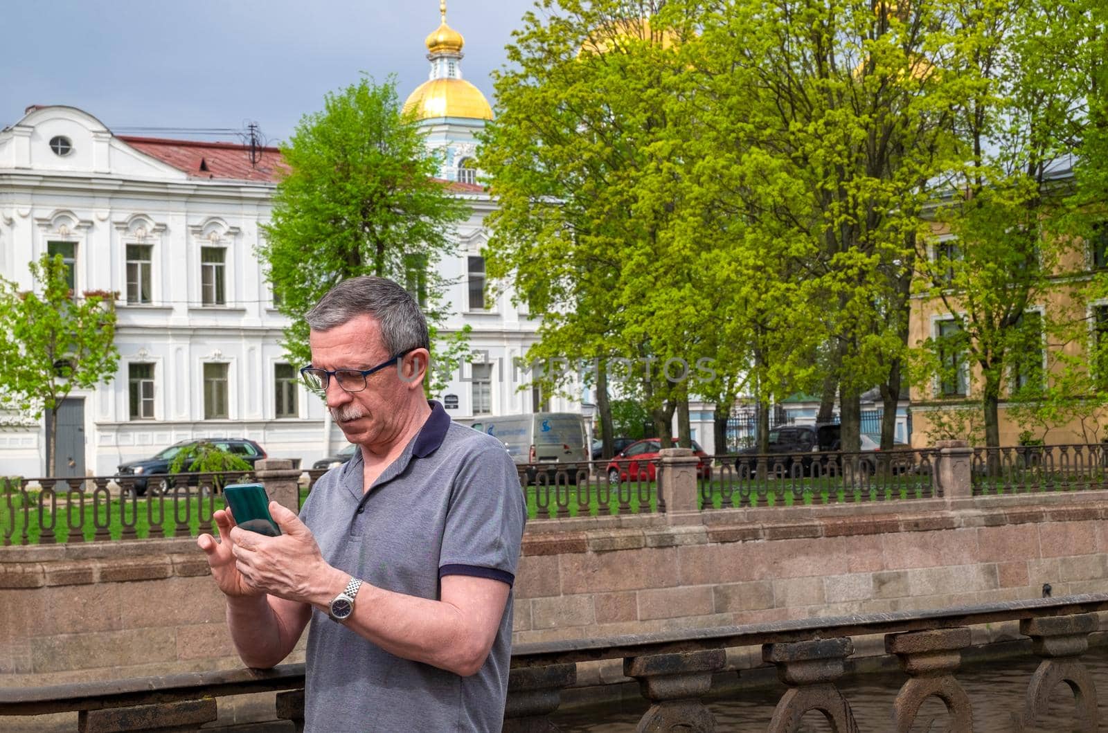 An adult caucasian senior man in a T-shirt is typing a message on a smartphone by OlgaGubskaya