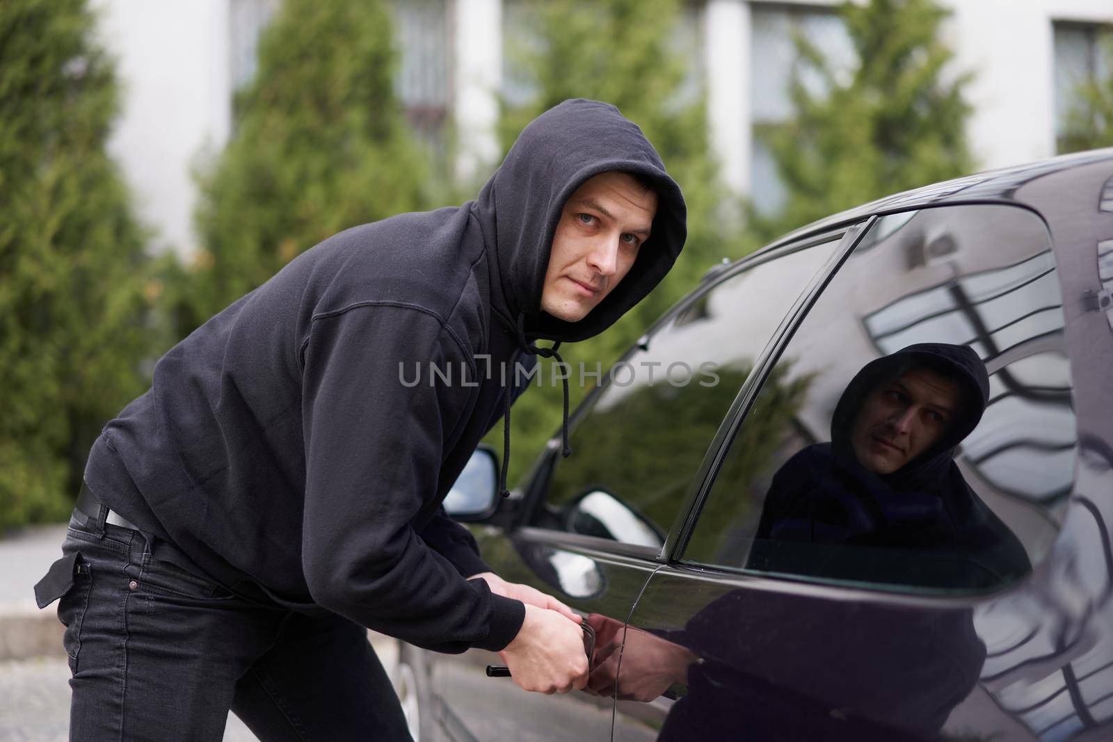 Car jacking thief steal car breaking door criminal job burglar Hijacks Auto thief black balaclava hoodie trying break into vehicle screwdriver Street crime violence gangster robber automobile parking