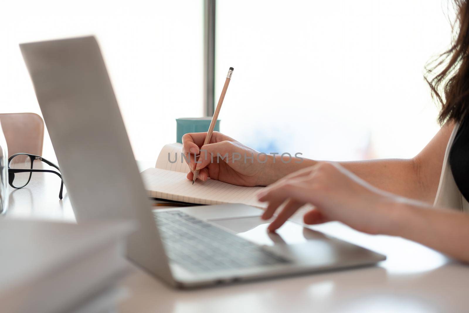 Close up woman's hands with laptop computer, notebook and pen taking notes in business office.