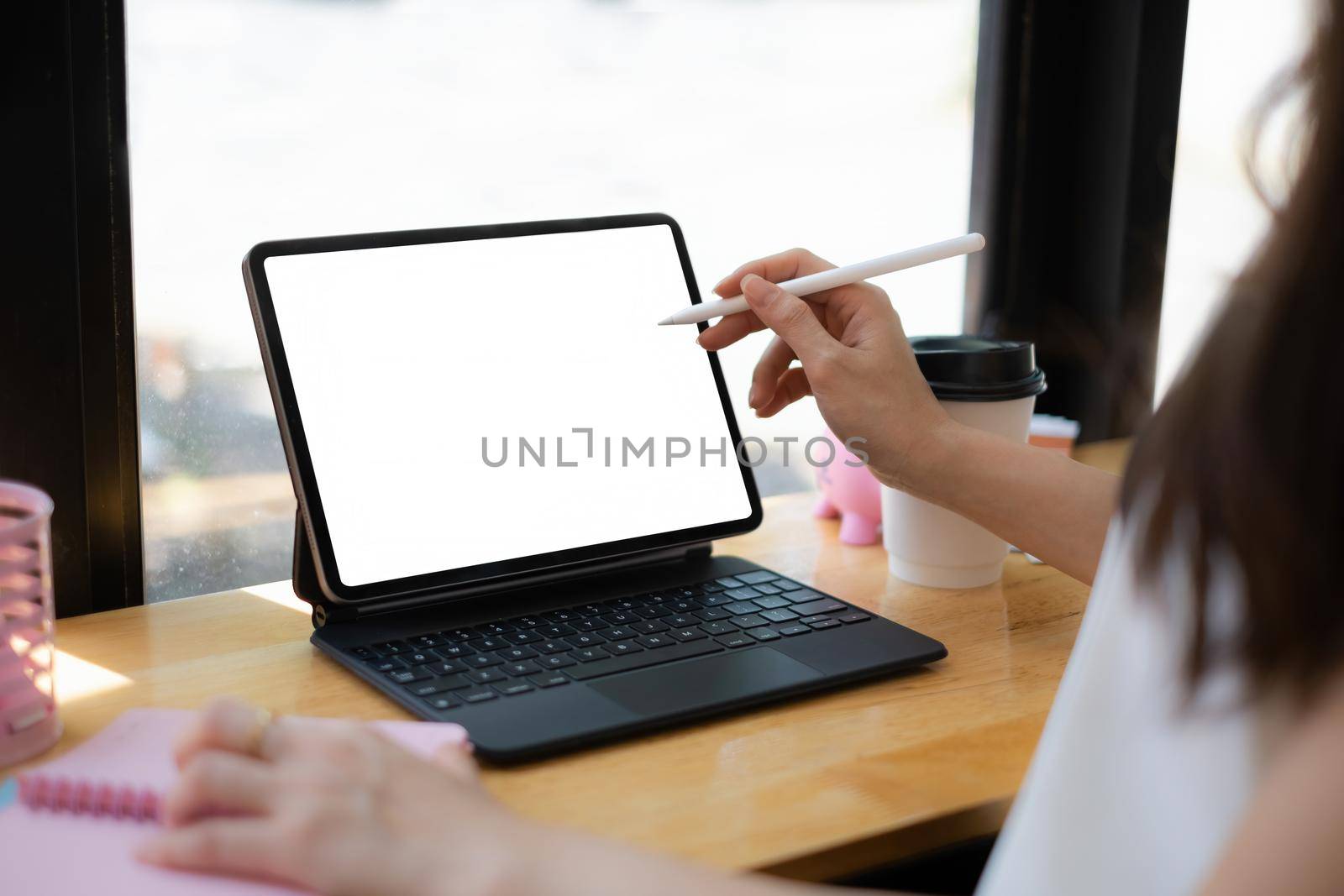 Mockup image of a woman hand using stylus with a black tablet with white blank screen on wooden desk