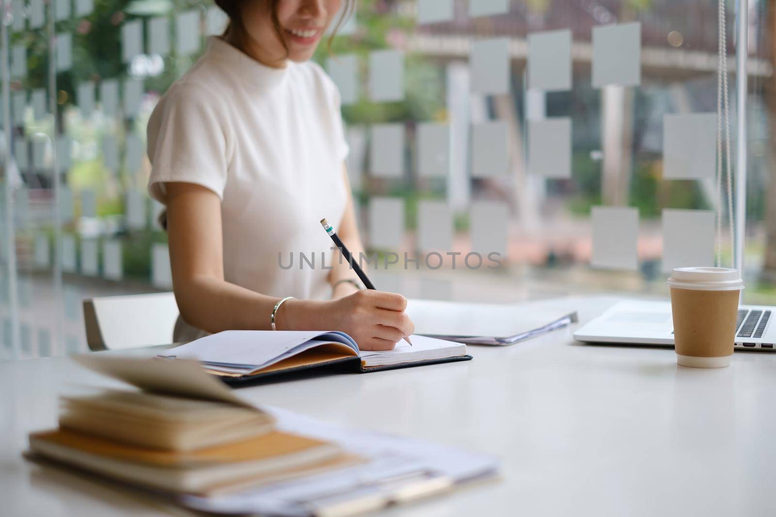 Young female college taking notes and using highlighter. Focused student in online class room. Authentic Education concept. by itchaznong