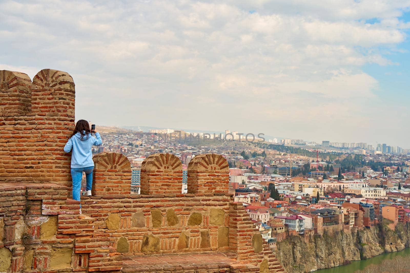 The girl enjoys the view and the silence while sitting on the wall of an ancient fortress overlooking the city.