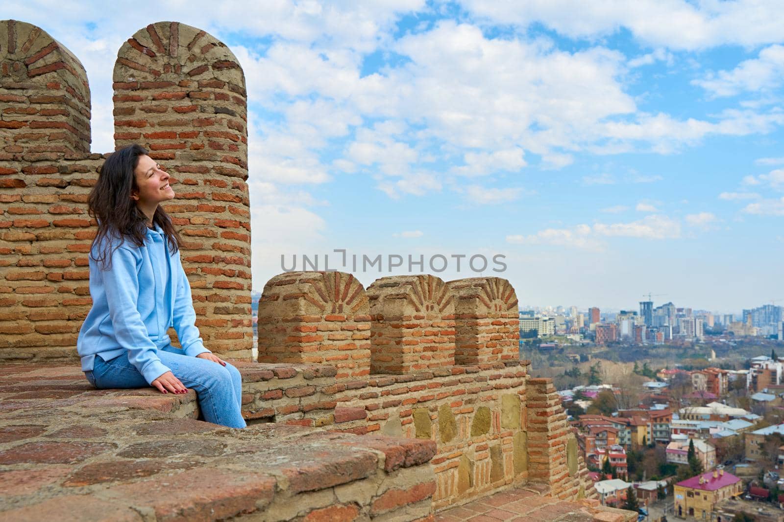 The girl enjoys the view and the silence while sitting on the wall of an ancient fortress overlooking the city by Try_my_best