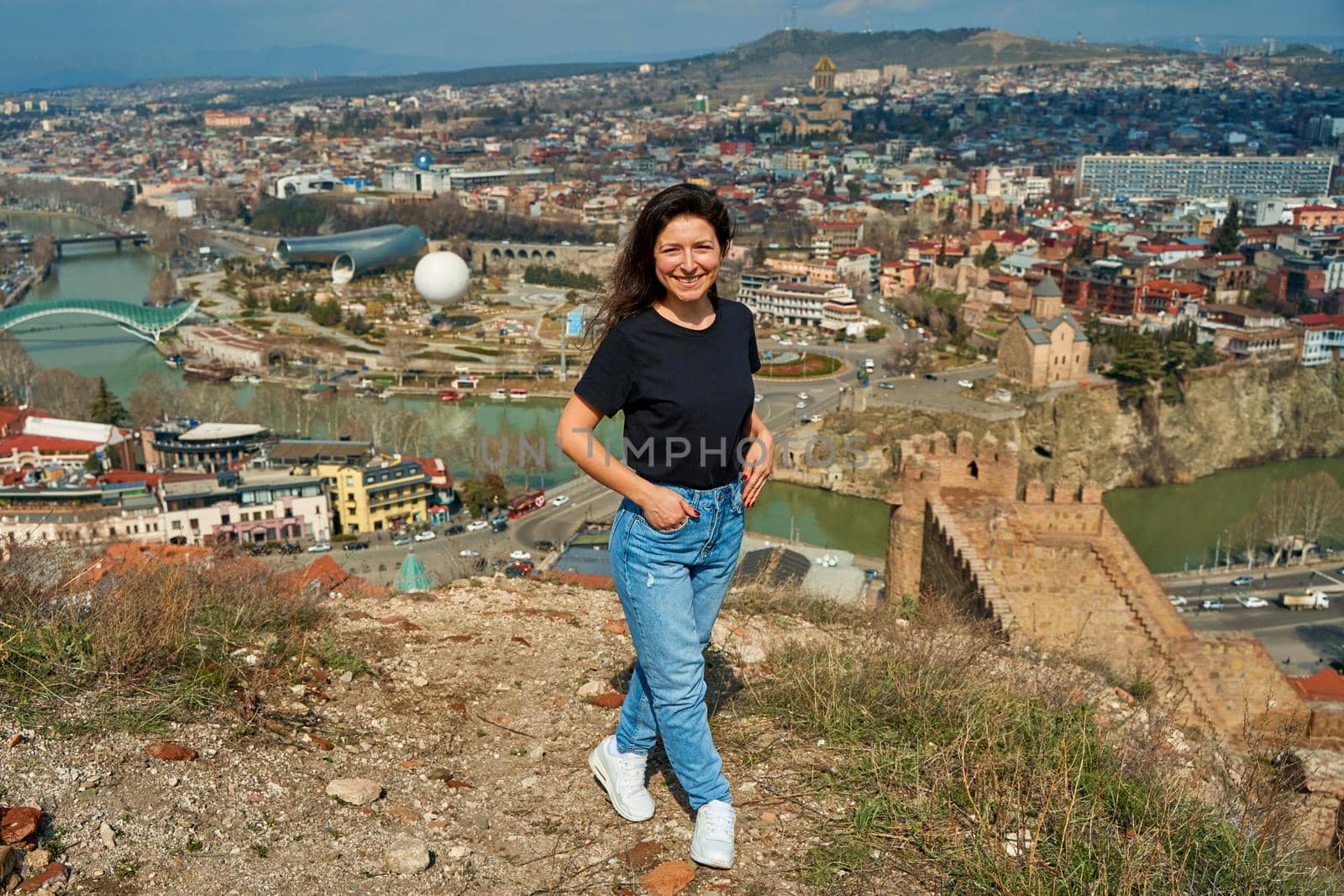 A cute brunette girl enjoys the stunning scenery of Tbilisi from the hill. The whole city at her feet.