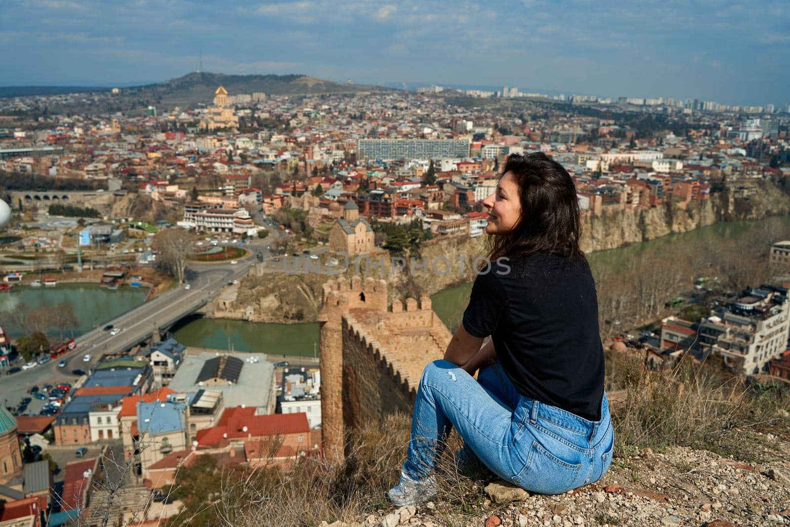 A cute brunette girl enjoys the stunning scenery of Tbilisi from the hill. The whole city at her feet.