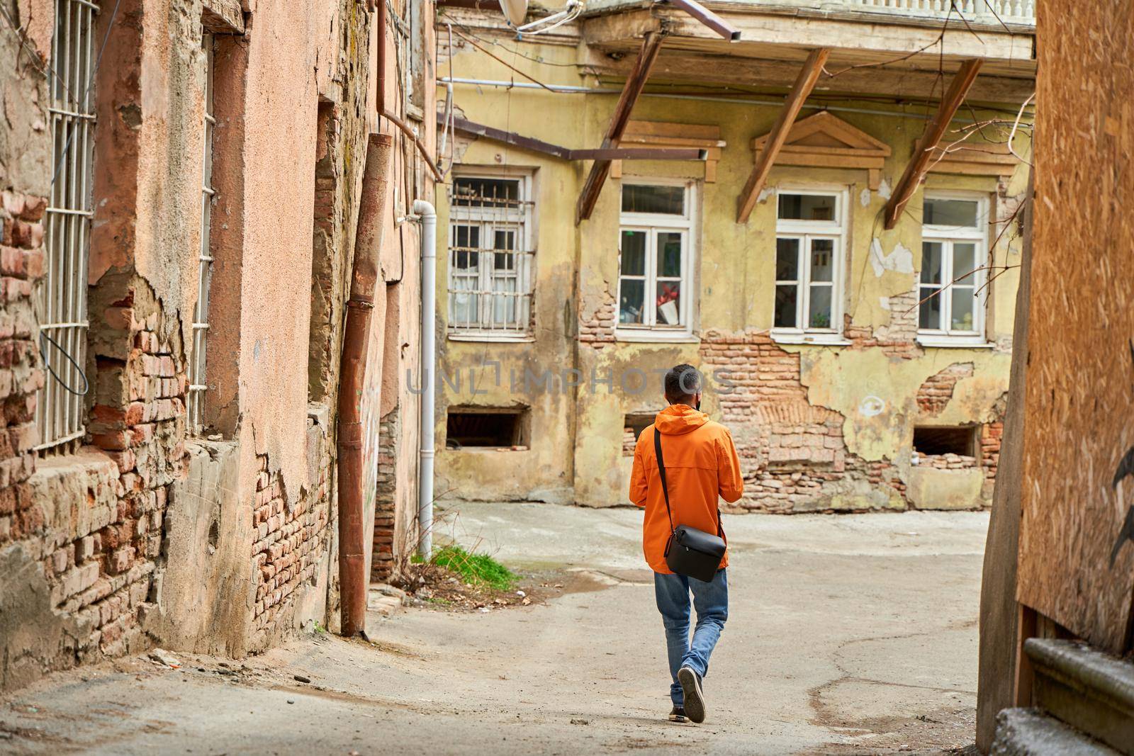 A lonely guy walks in the old part of the city between dilapidated houses.