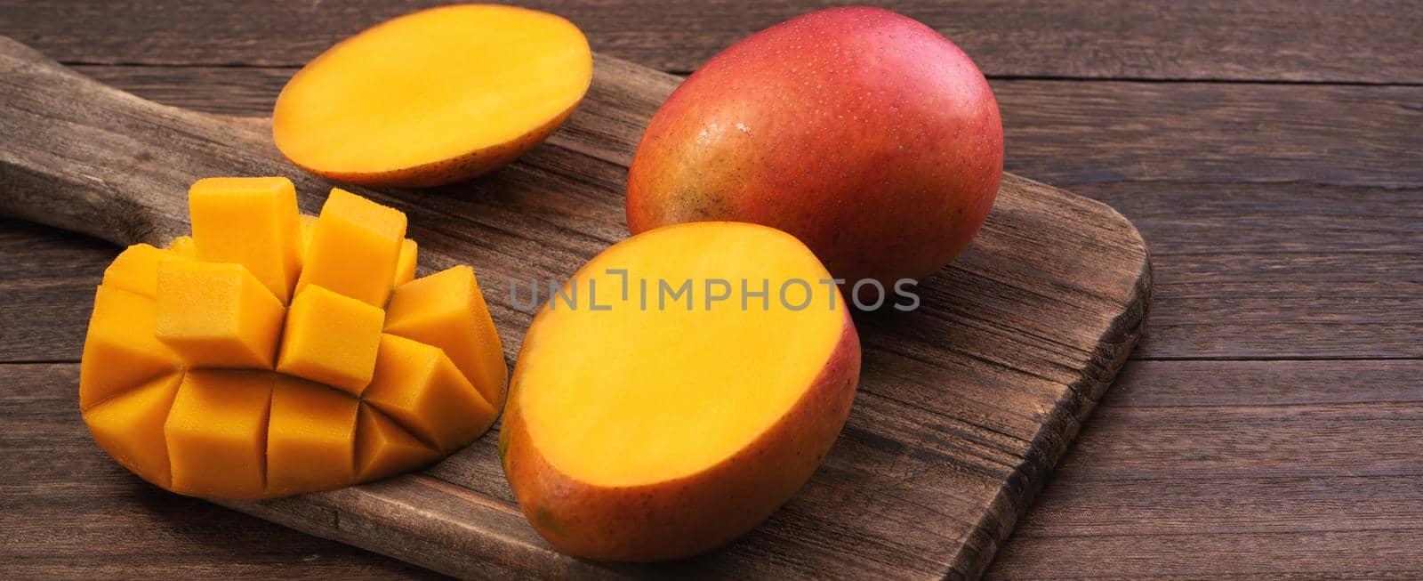 Mango. Close up of fresh ripe mango fruit with leaves over dark wooden table background with green leaves.