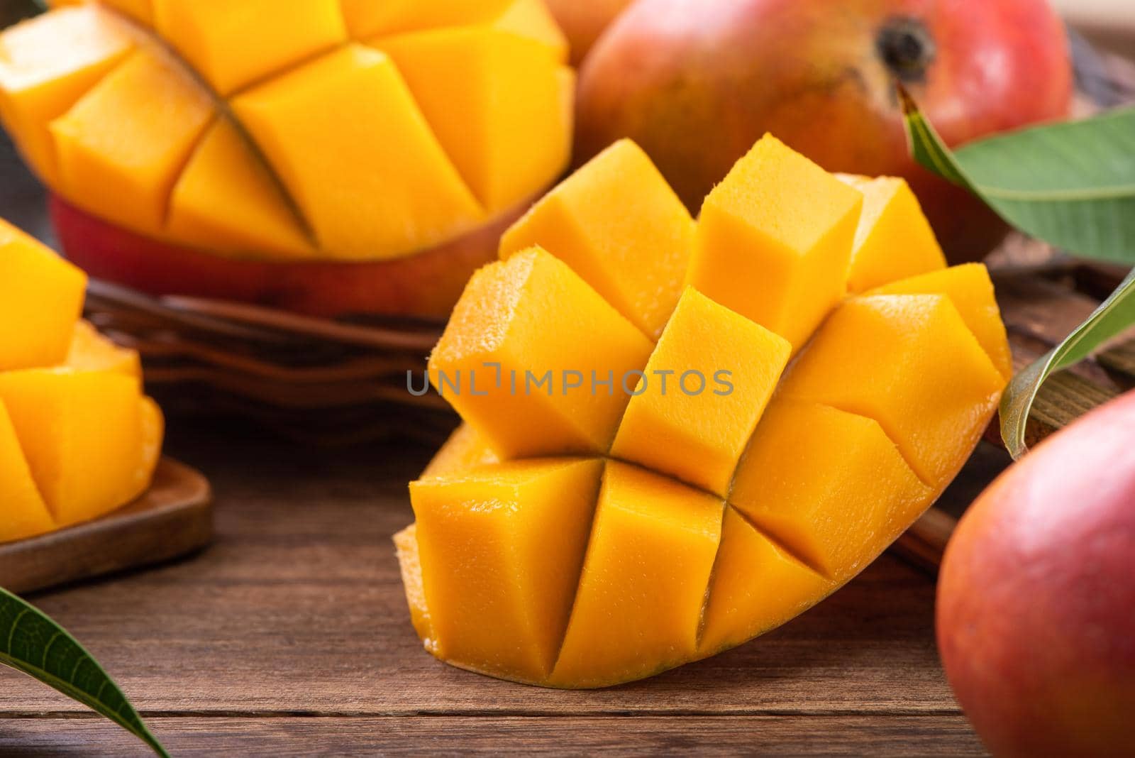 Mango. Close up of fresh ripe mango fruit with leaves over dark wooden table background with green leaves.