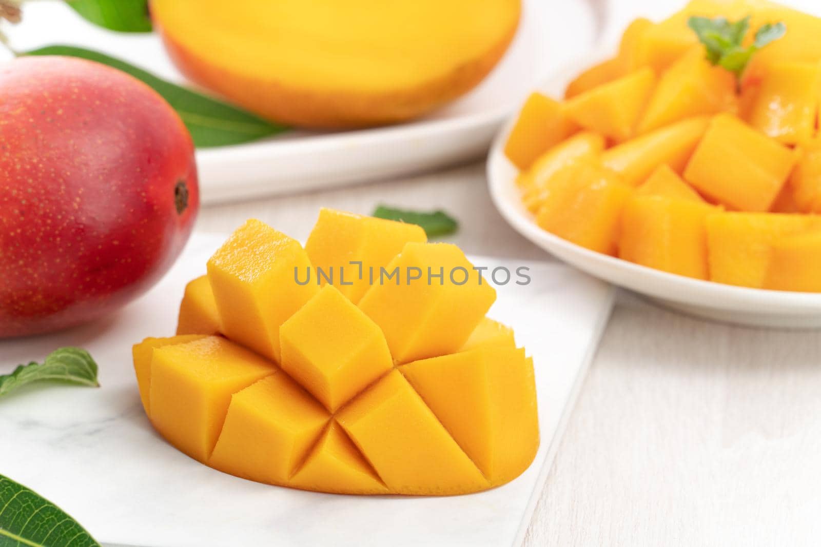 Diced fresh mango fruit on a white plate with leaves over wooden table background.