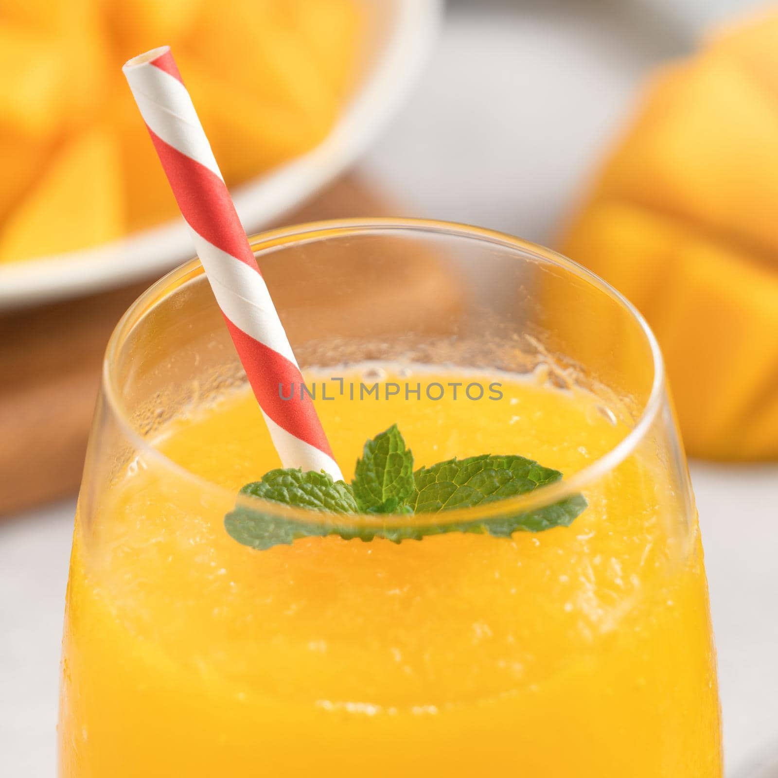 Fresh beautiful delicious mango juice. Close up design concept of smoothie cold drink in a glass cup with paper straw on gray table background.
