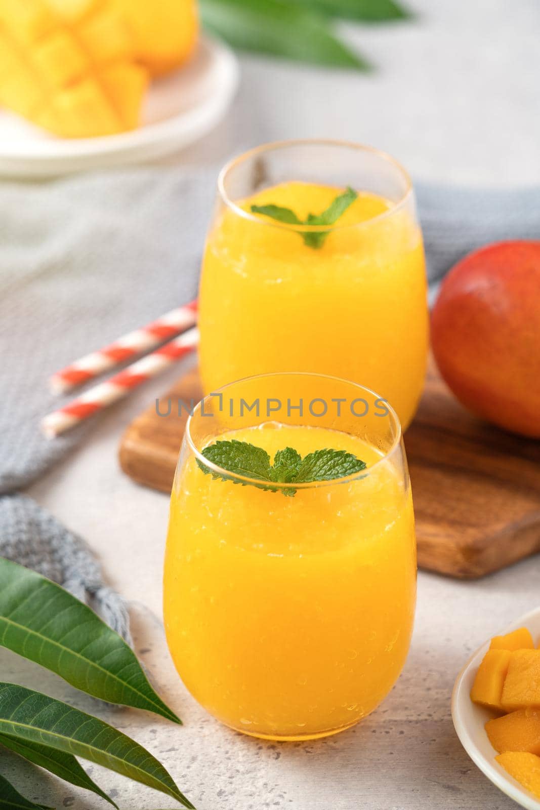 Fresh beautiful delicious mango juice. Close up design concept of smoothie cold drink in a glass cup with paper straw on gray table background.