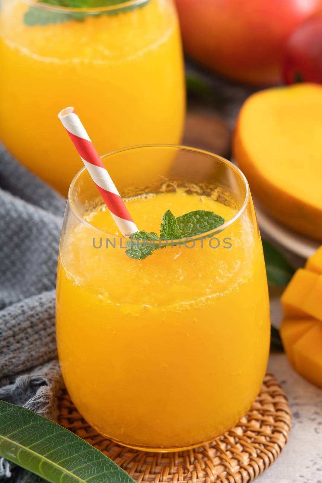 Fresh beautiful delicious mango juice. Close up design concept of smoothie cold drink in a glass cup with paper straw on gray table background.