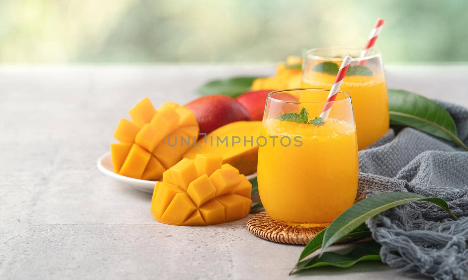 Fresh beautiful delicious mango juice. Close up design concept of smoothie cold drink in a glass cup with paper straw on gray table background.
