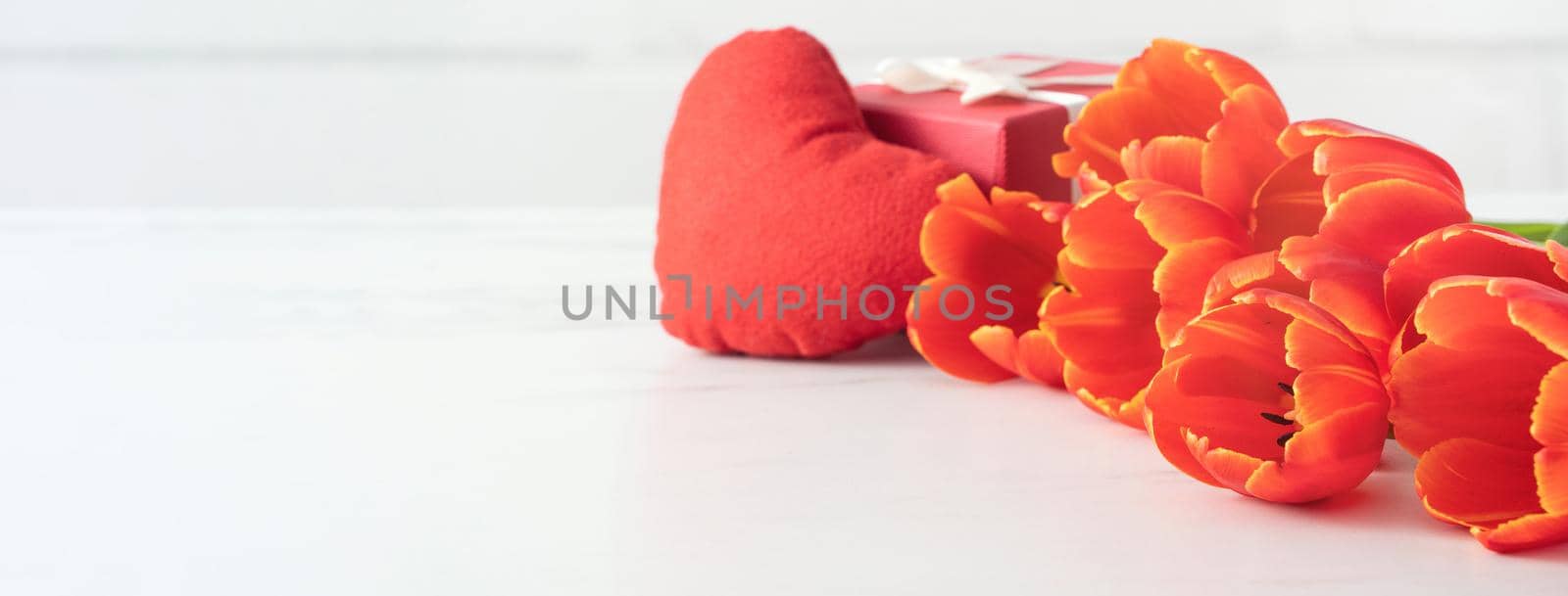 Mother's Day gift. Close up design concept of red tulip bouquet with gift and heart shape on white table background and brick wall decoration.