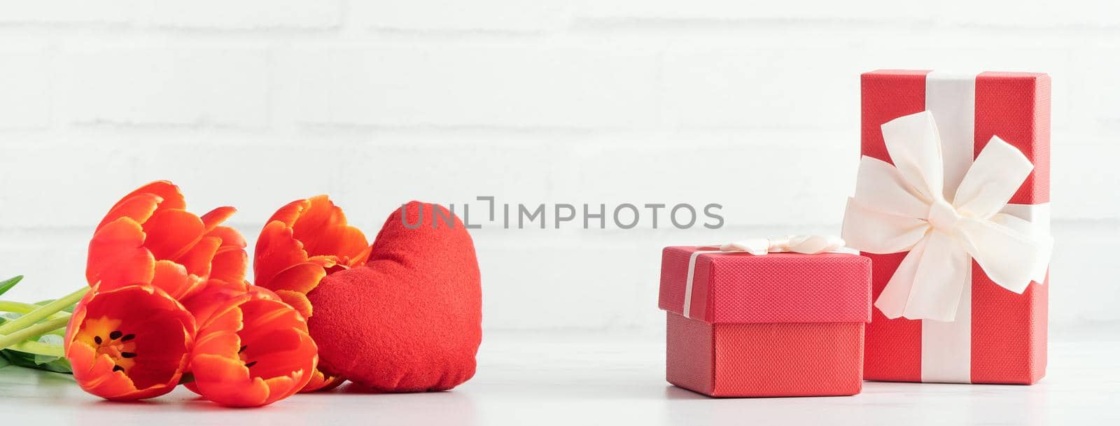 Mother's Day gift. Close up design concept of red tulip bouquet with gift and heart shape on white table background and brick wall decoration.