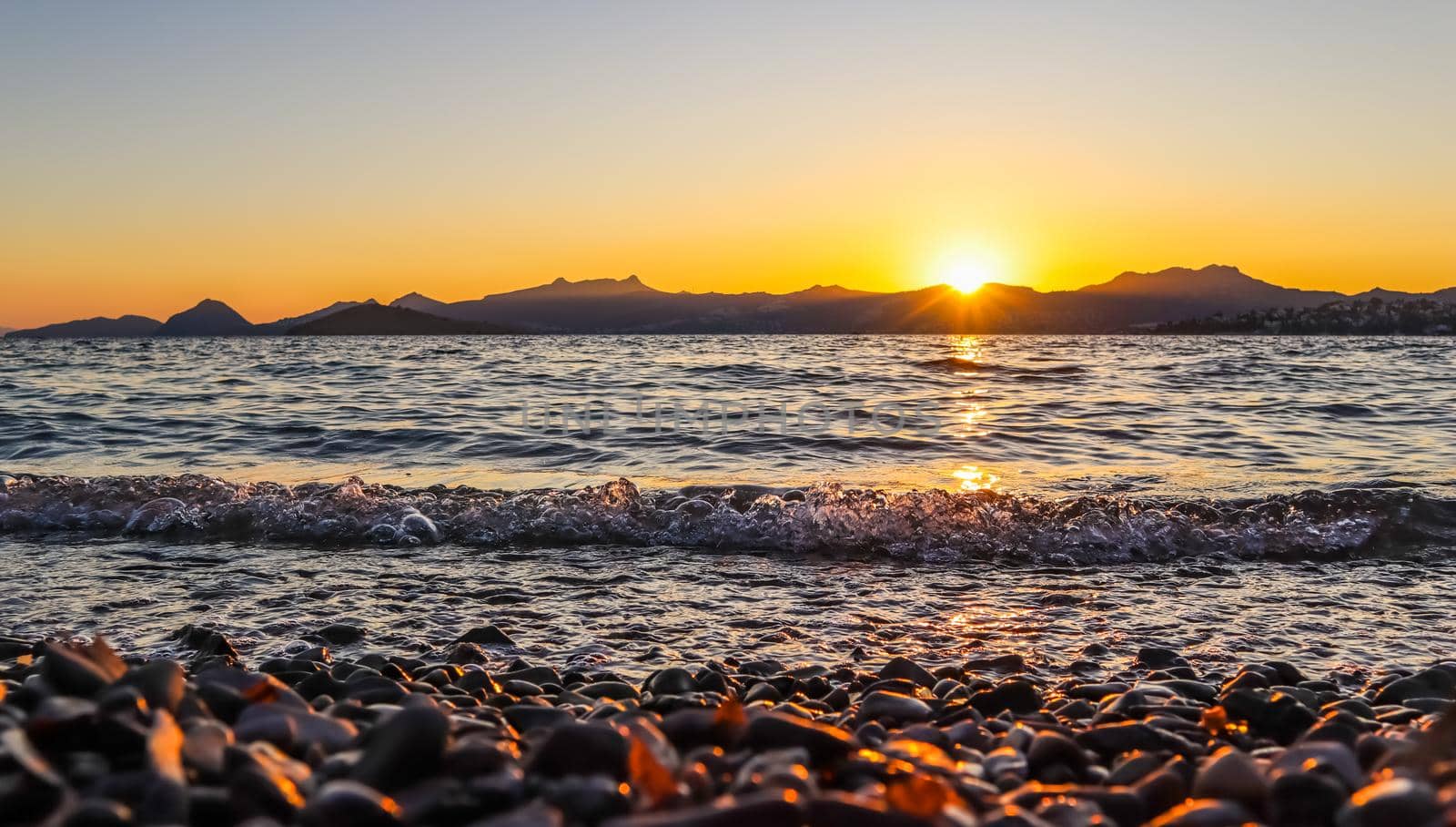 Beautiful sunset on the Mediterranean coast with islands and mountains. Stones on the beach lit by sunlight