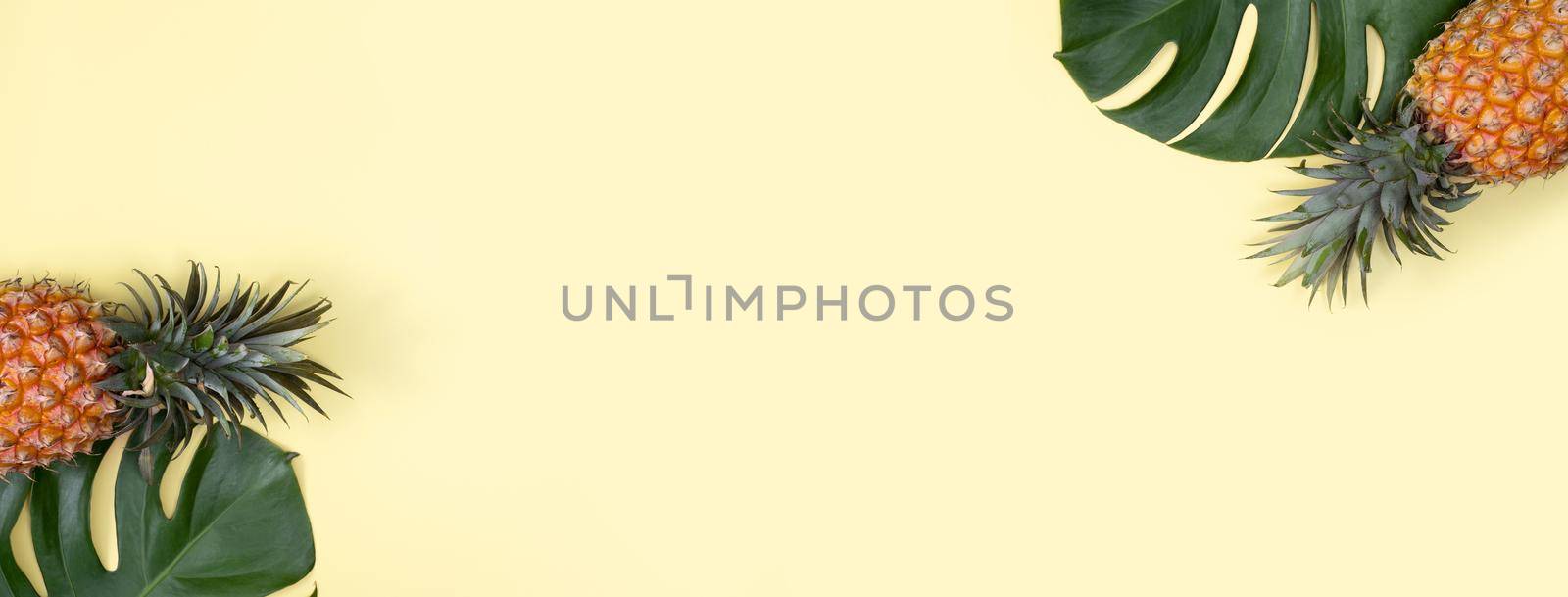 Top view of fresh pineapple with tropical palm and monstera leaves on yellow table background.