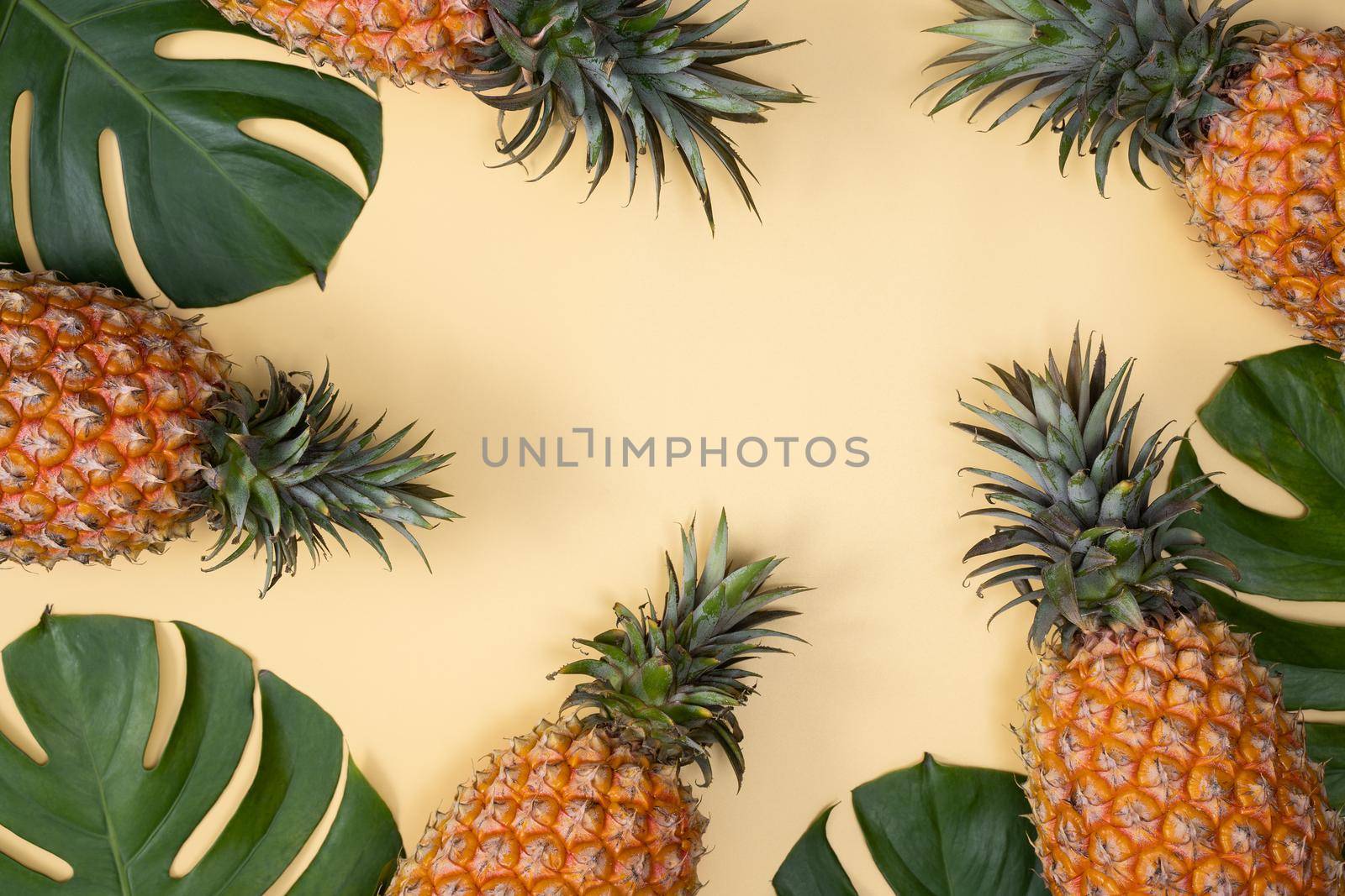 Top view of fresh pineapple with tropical leaves on yellow background. by ROMIXIMAGE