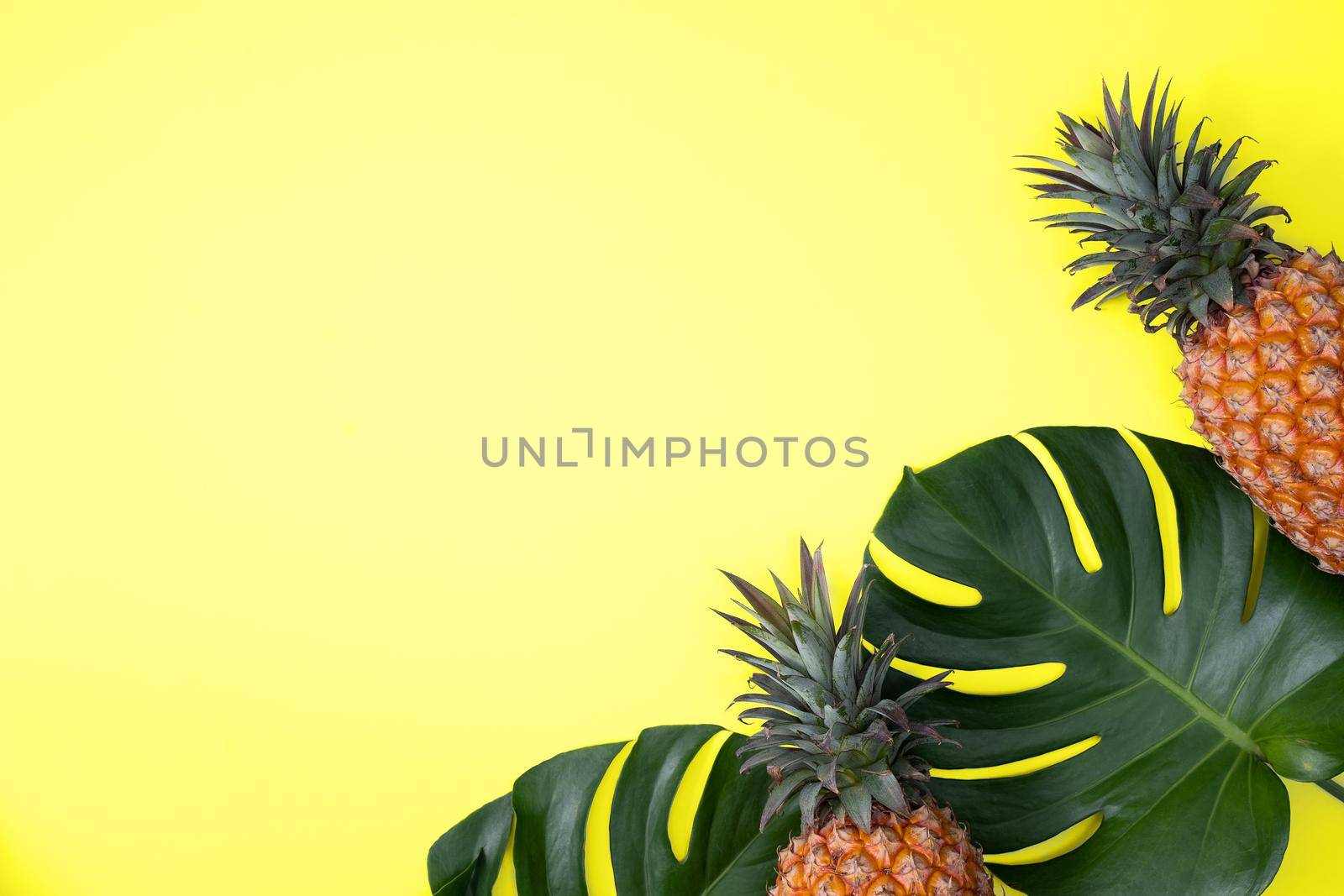 Top view of fresh pineapple with tropical palm and monstera leaves on yellow table background.