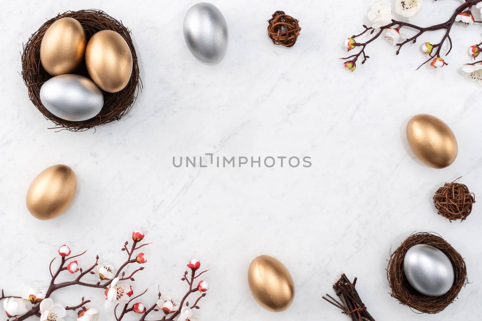 Design concept of Golden and silver Easter eggs in the nest with white plum flower on bright marble white table background.