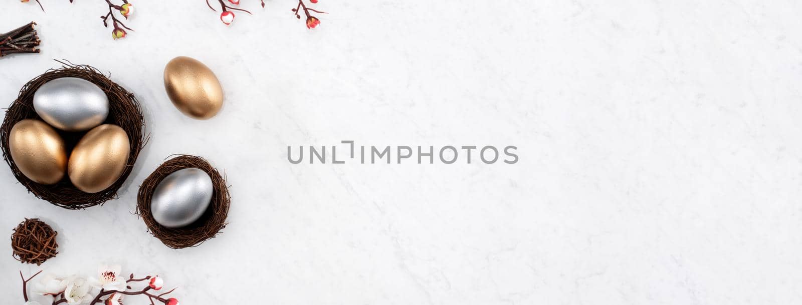 Design concept of Golden and silver Easter eggs in the nest with white plum flower on bright marble white table background.