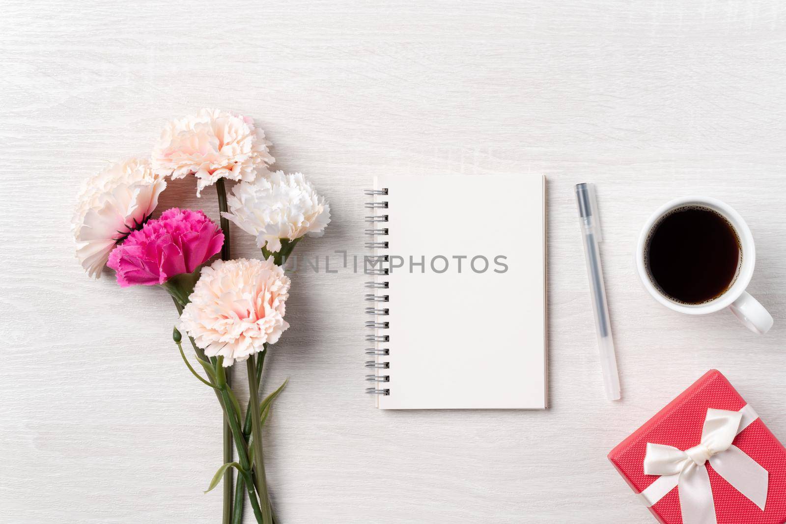 Design concpet of Mother's Day greeting with carnation flower, holiday gift idea and notebook diary on mother's desk background.
