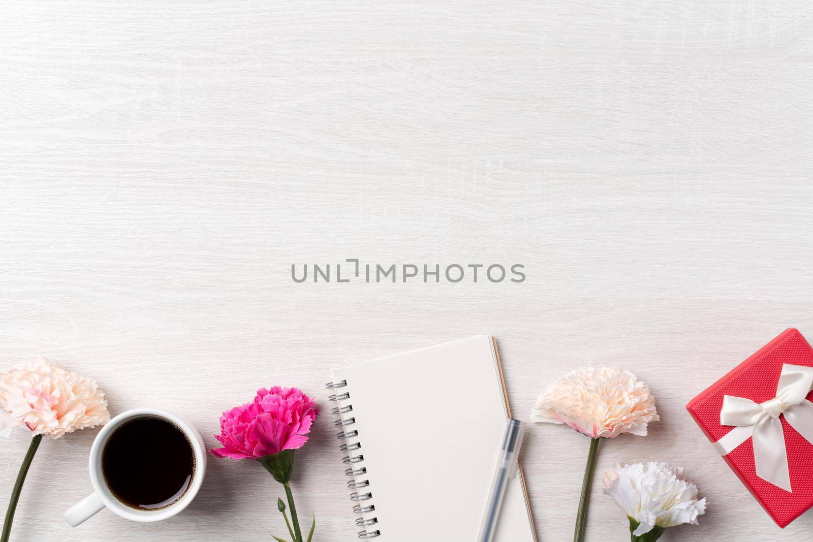 Design concpet of Mother's Day greeting with carnation flower, holiday gift idea and notebook diary on mother's desk background.