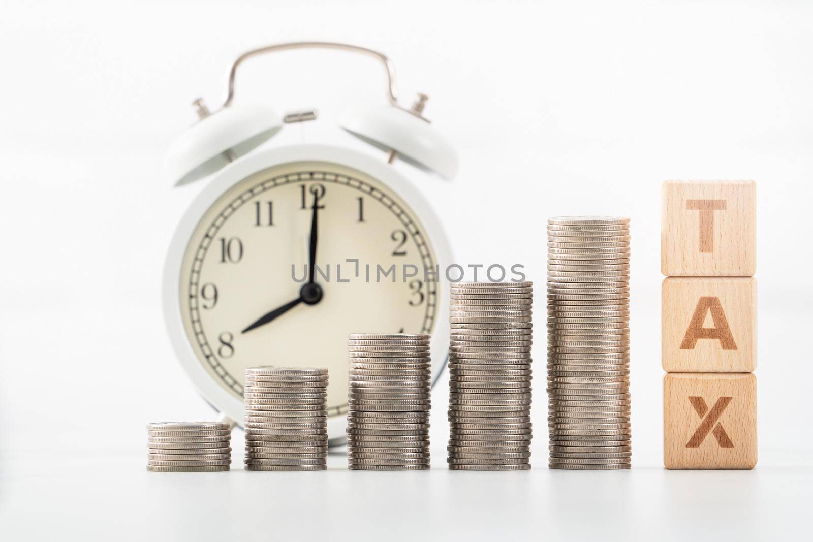 Concept of tax season approaching with wooden blocks, coins and alarm clock over white background.