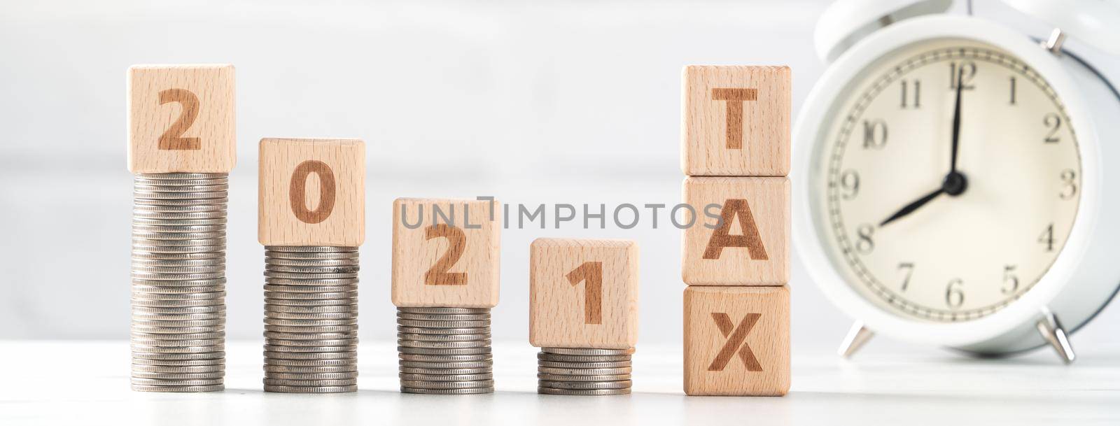 Concept of tax season approaching with wooden blocks, coins and alarm clock over white background.