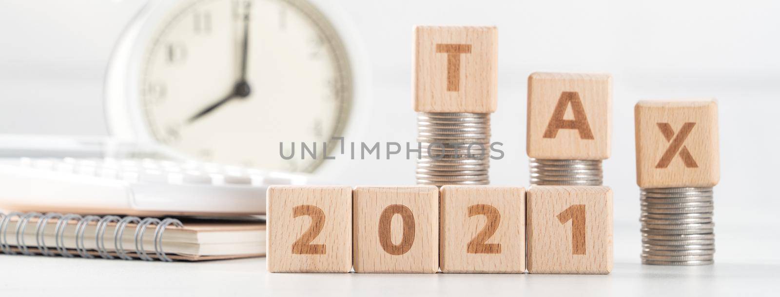 Concept of tax season approaching with wooden blocks, coins and alarm clock over white background.