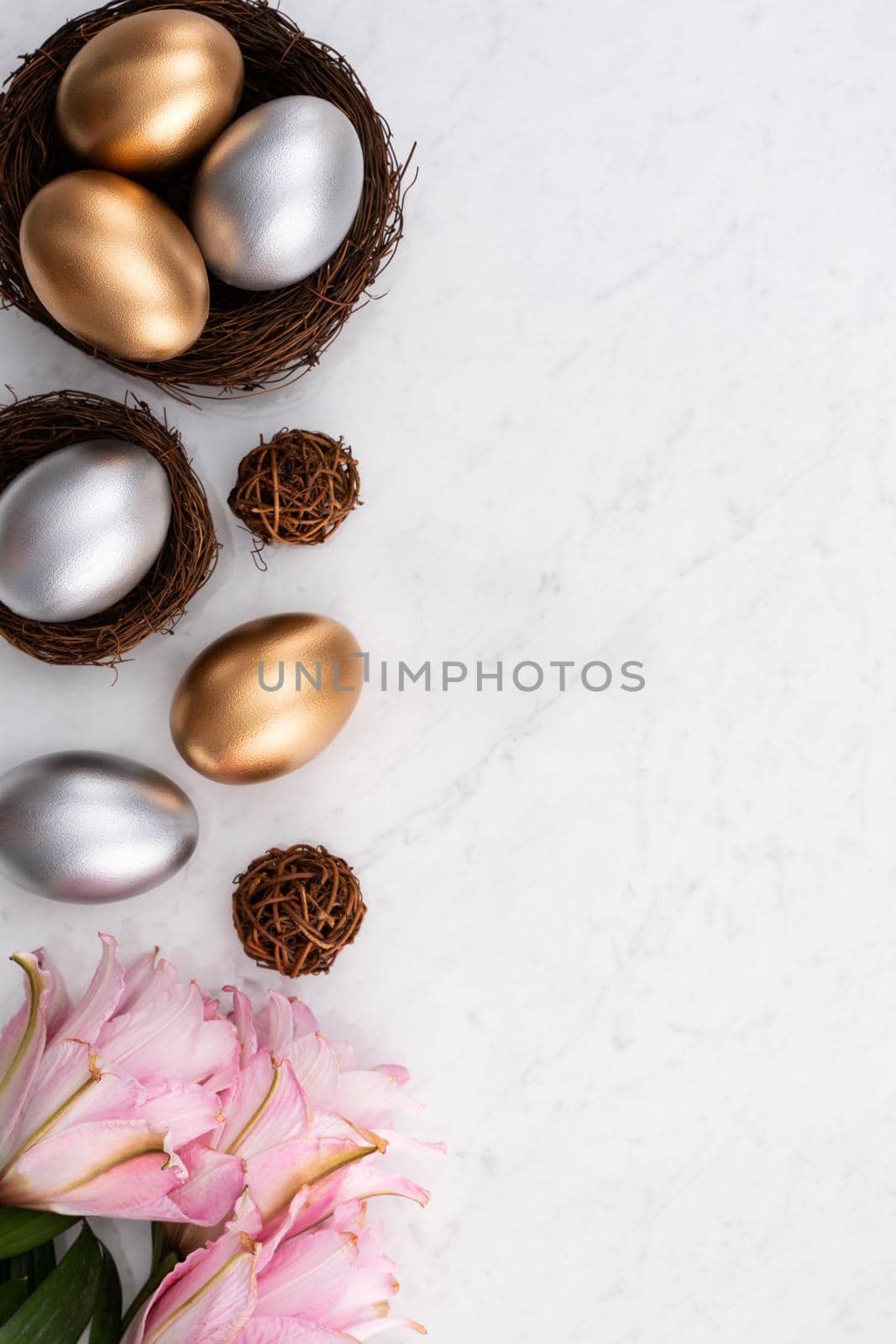 Design concept of Golden and silver Easter eggs in the nest with pink lily flower on bright marble white table background.